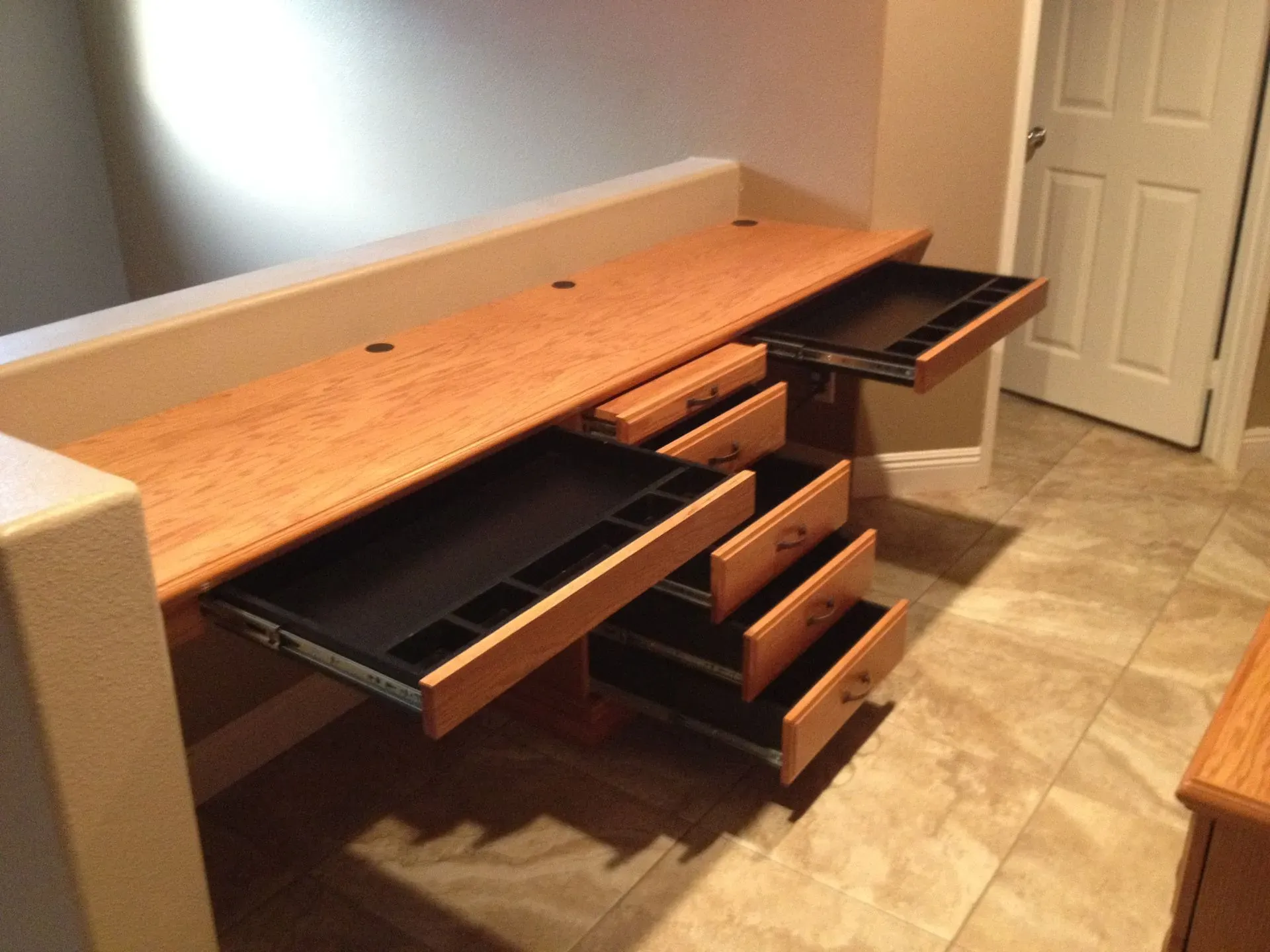 Wooden computer desk with open drawers in a tiled room near a white door.