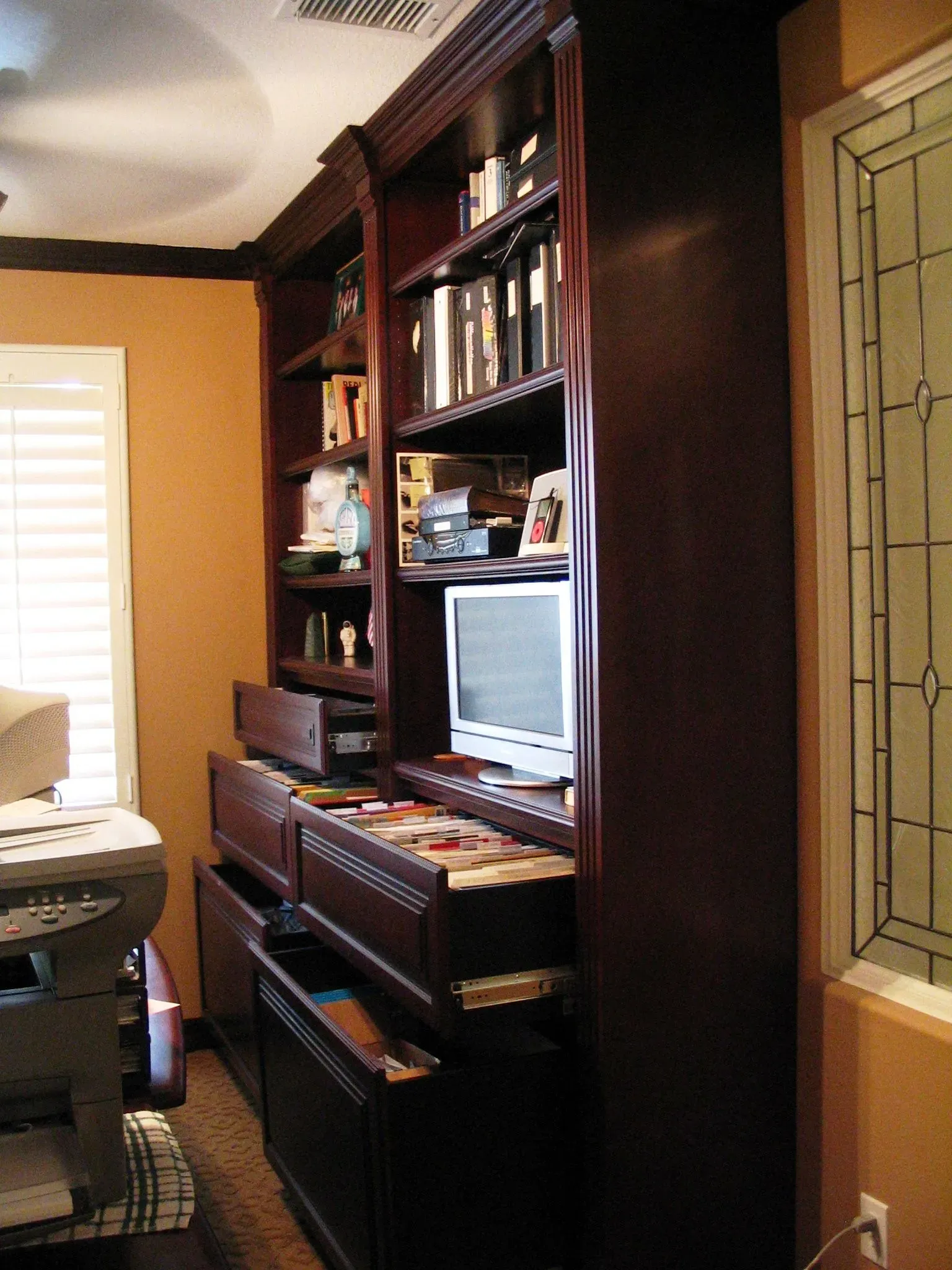 Home office corner with dark wood shelves, a computer monitor, and a piano keyboard against warm walls