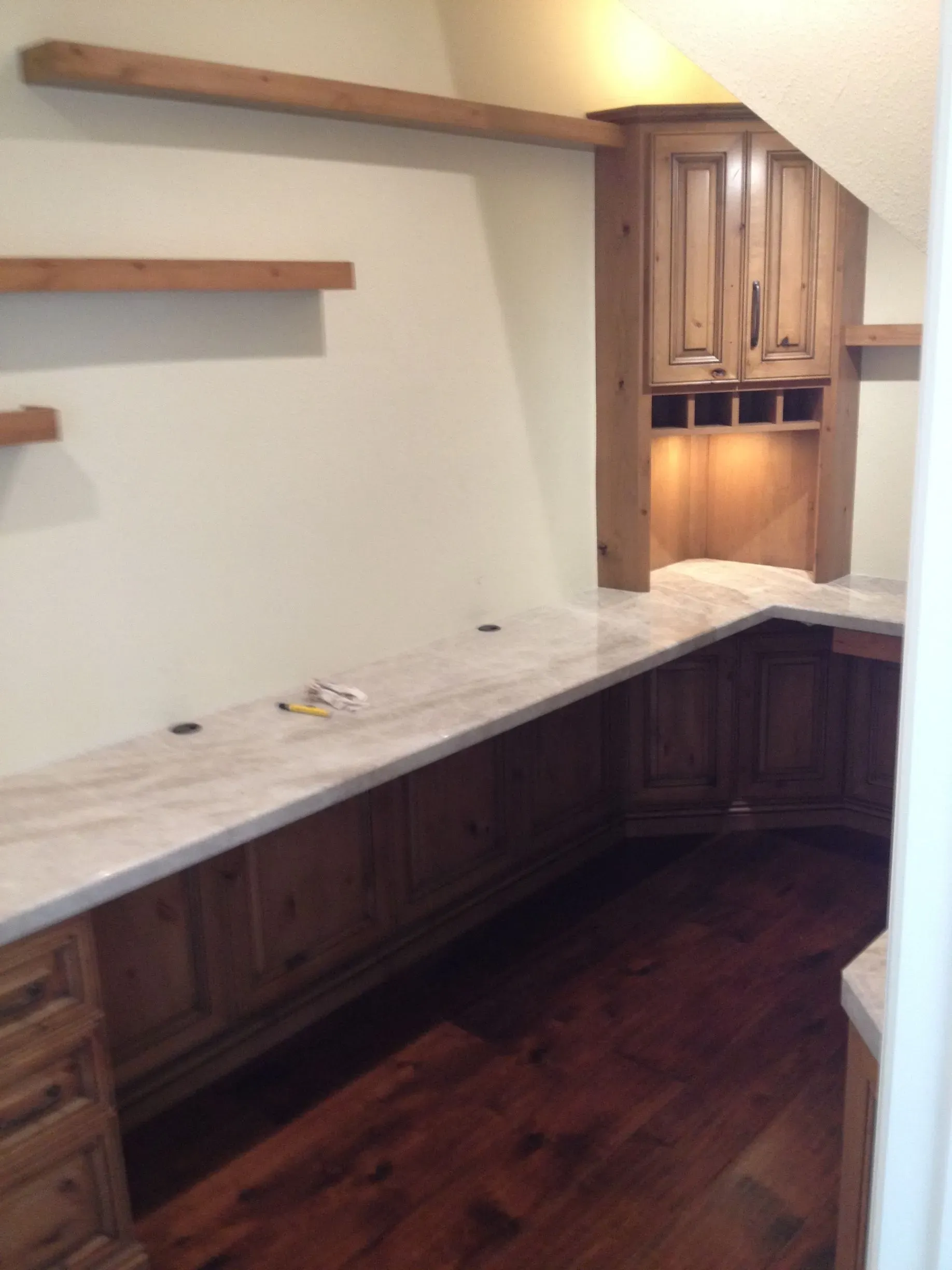 Empty built-in wooden desk with marble top in a small room with shelves and under-cabinet lighting