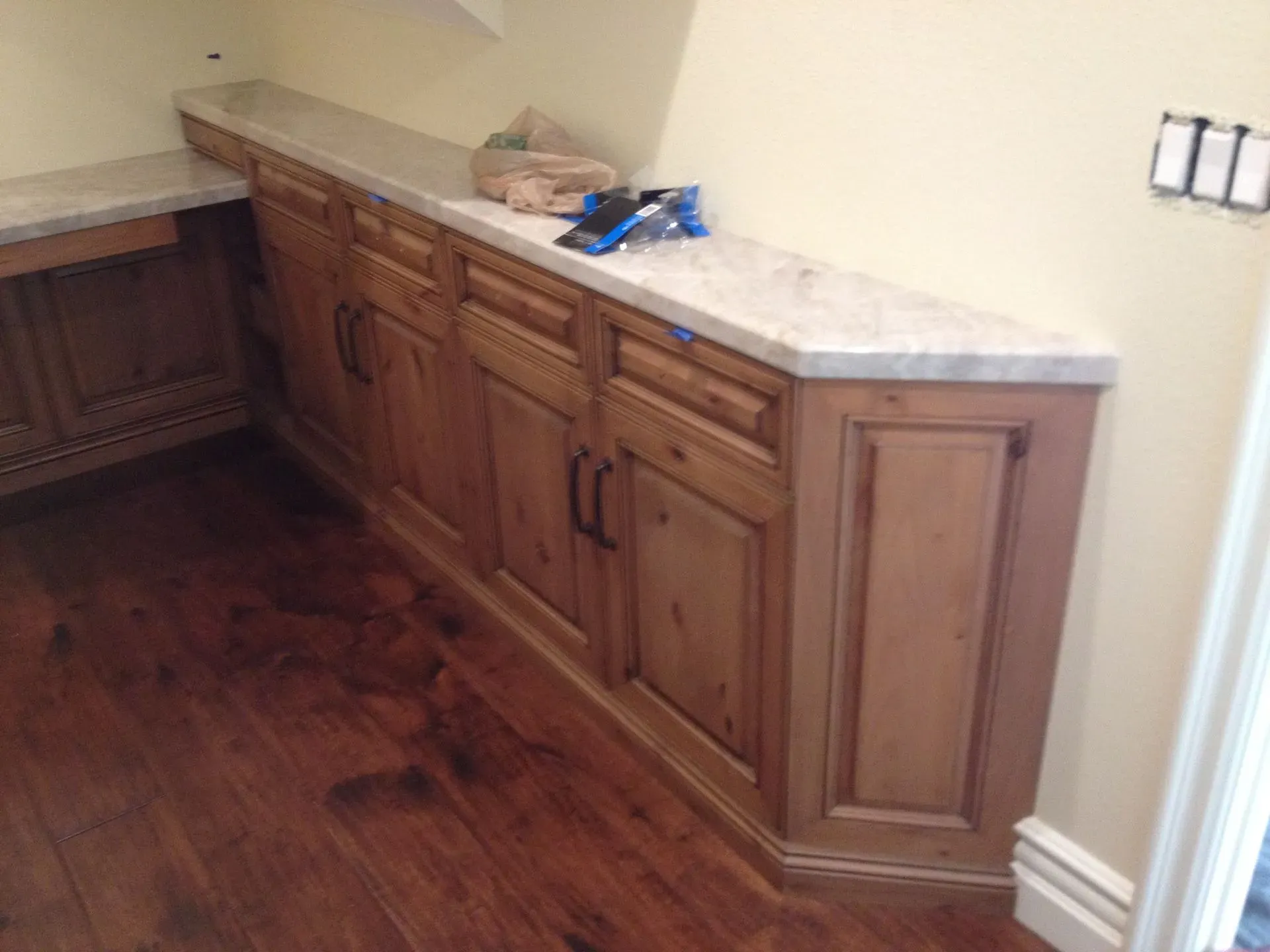 Wooden kitchen cabinets with marble countertop and hardwood floor in a corner alcove.