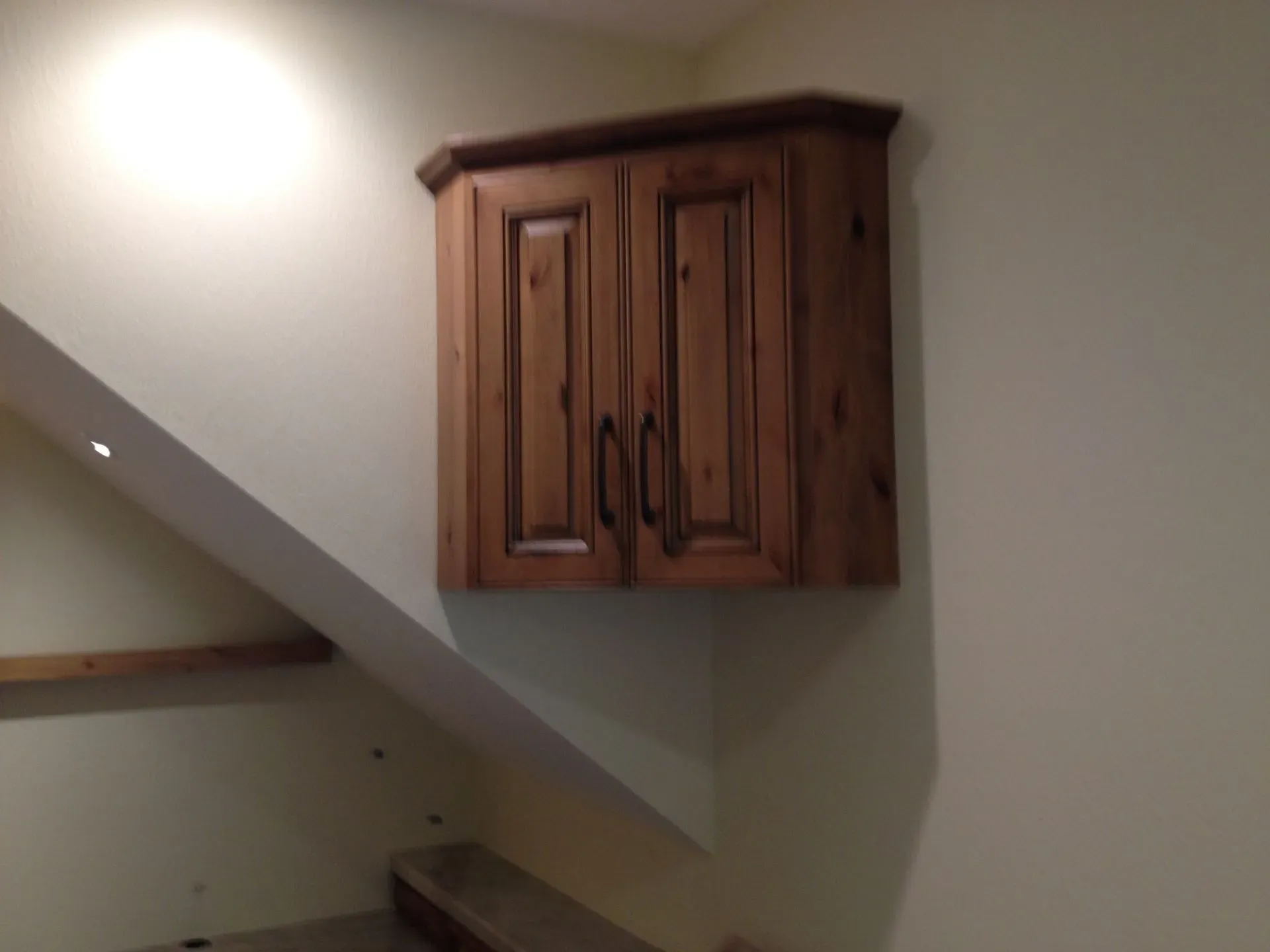 Wooden wall cabinet mounted on a beige staircase wall with a slanted ceiling.