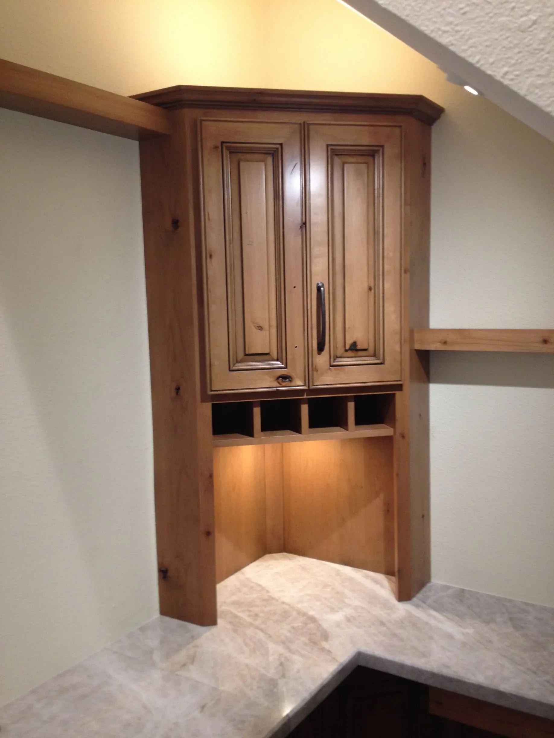 Built-in wooden corner cabinet with under-cabinet lighting in a room with sloped ceiling.