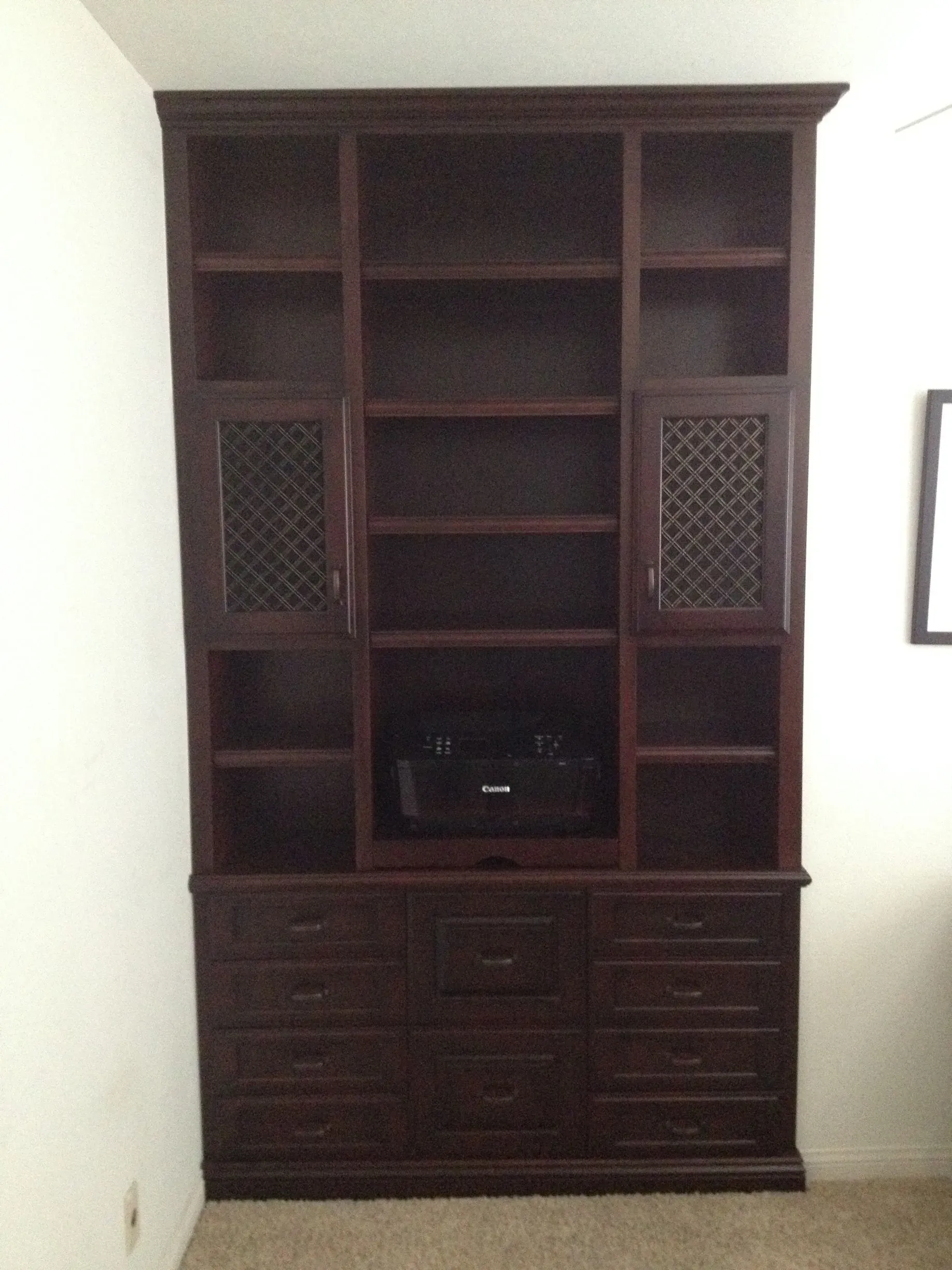 Dark wooden entertainment cabinet with shelves, lattice side panels, and drawers against a white wall.