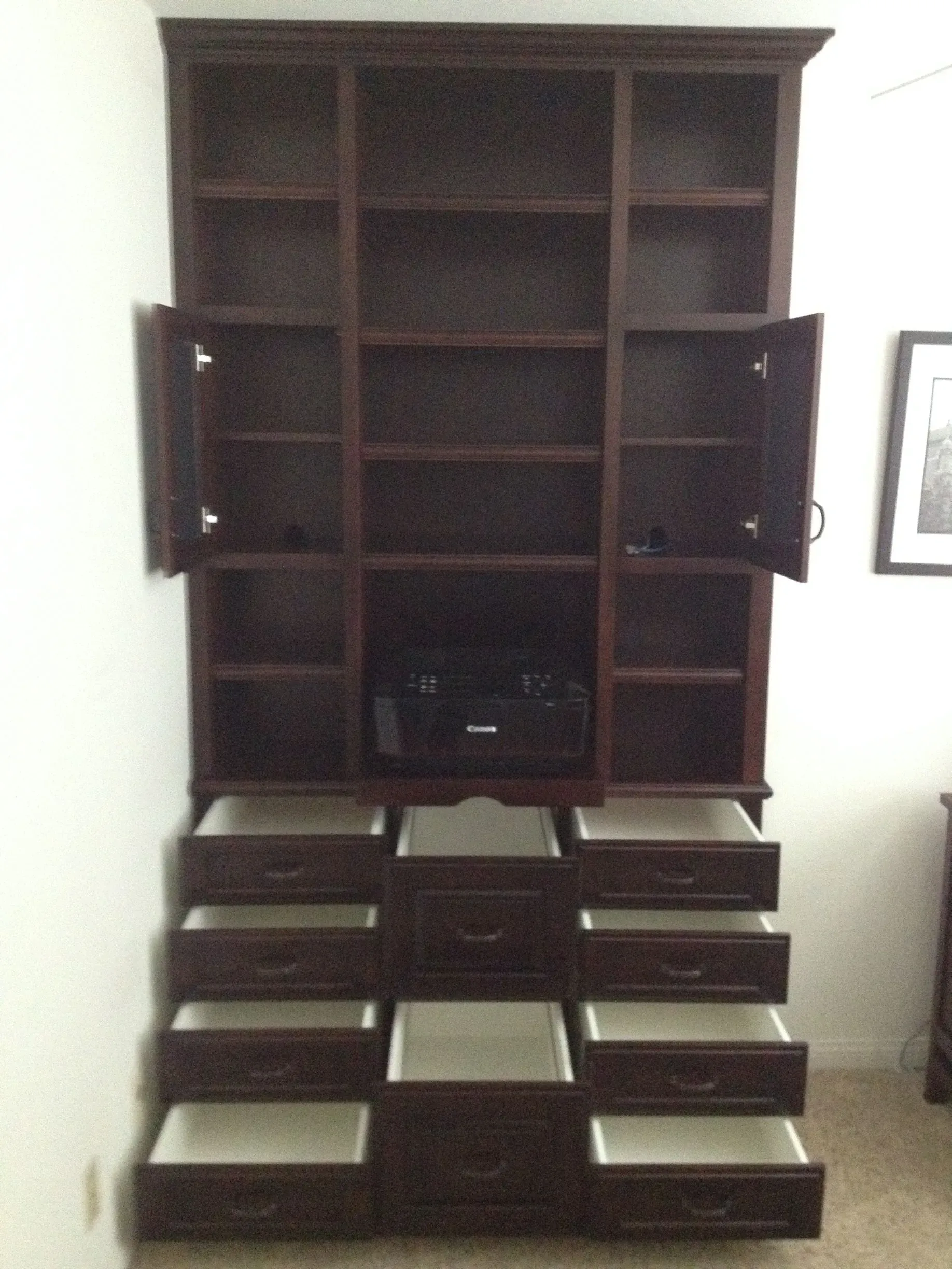 Dark wooden wall cabinet with open doors and many small drawers, centered against a light wall.