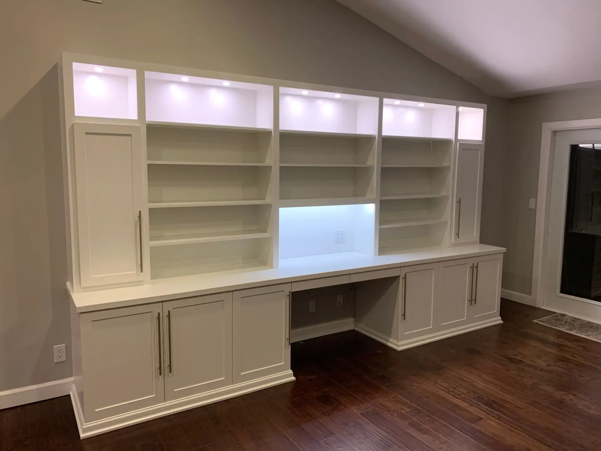 Built-in white cabinetry and bookshelves with under-cabinet lighting in a room with hardwood floors