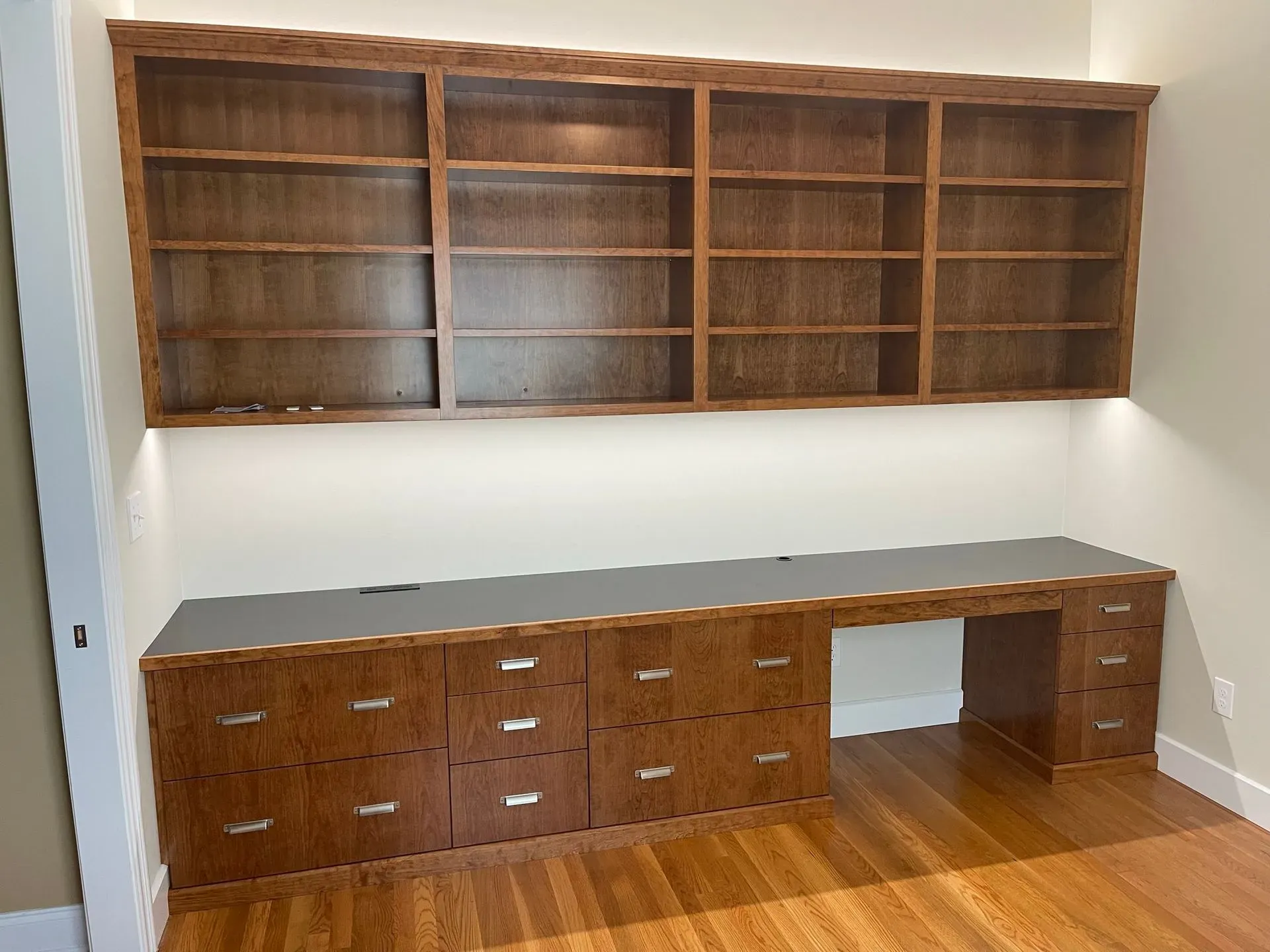 Wooden wall shelves and a long wooden desk with drawers in a bare office room