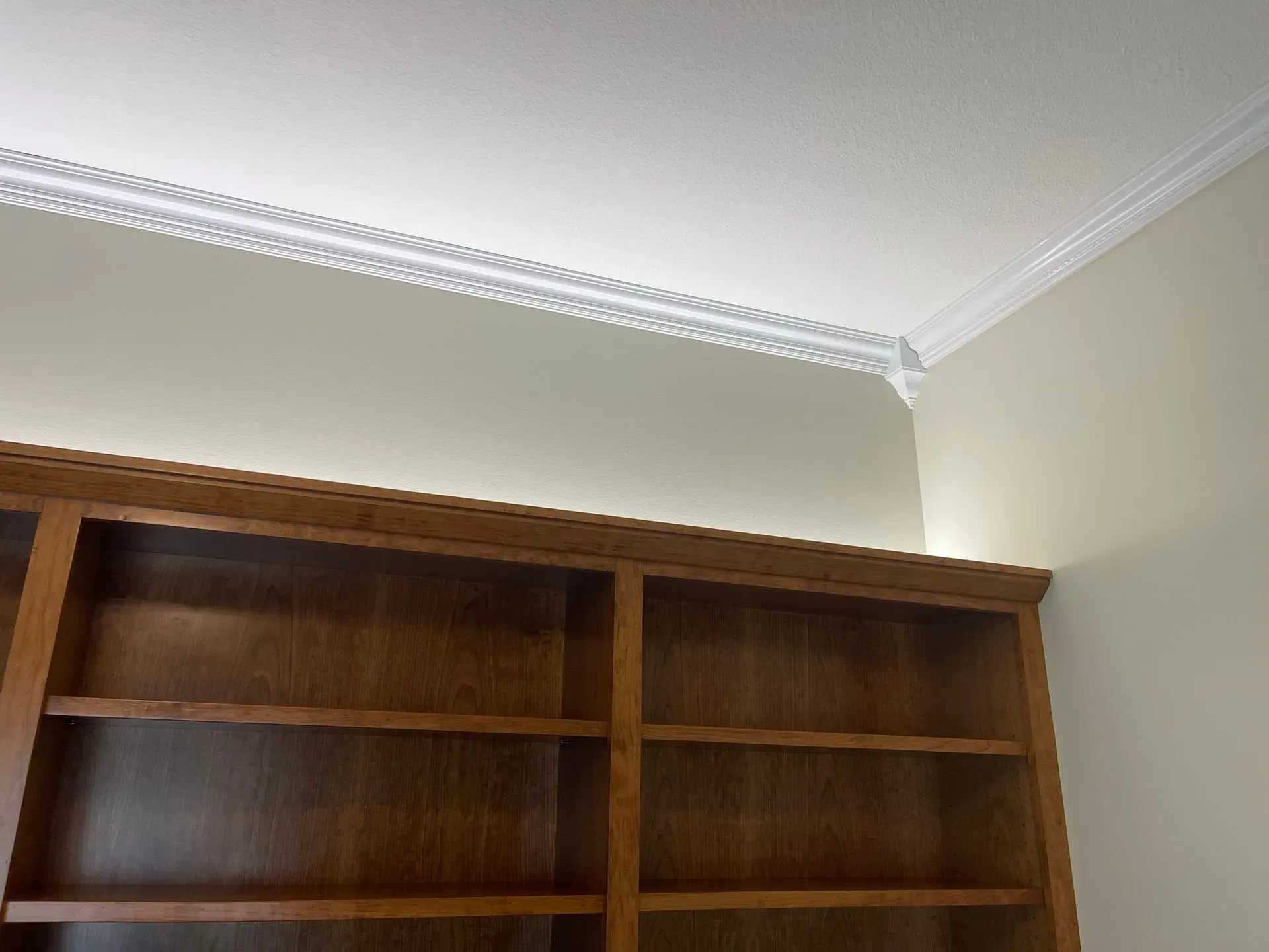 Wooden bookshelf beneath a cream wall with white crown molding in a corner of a room