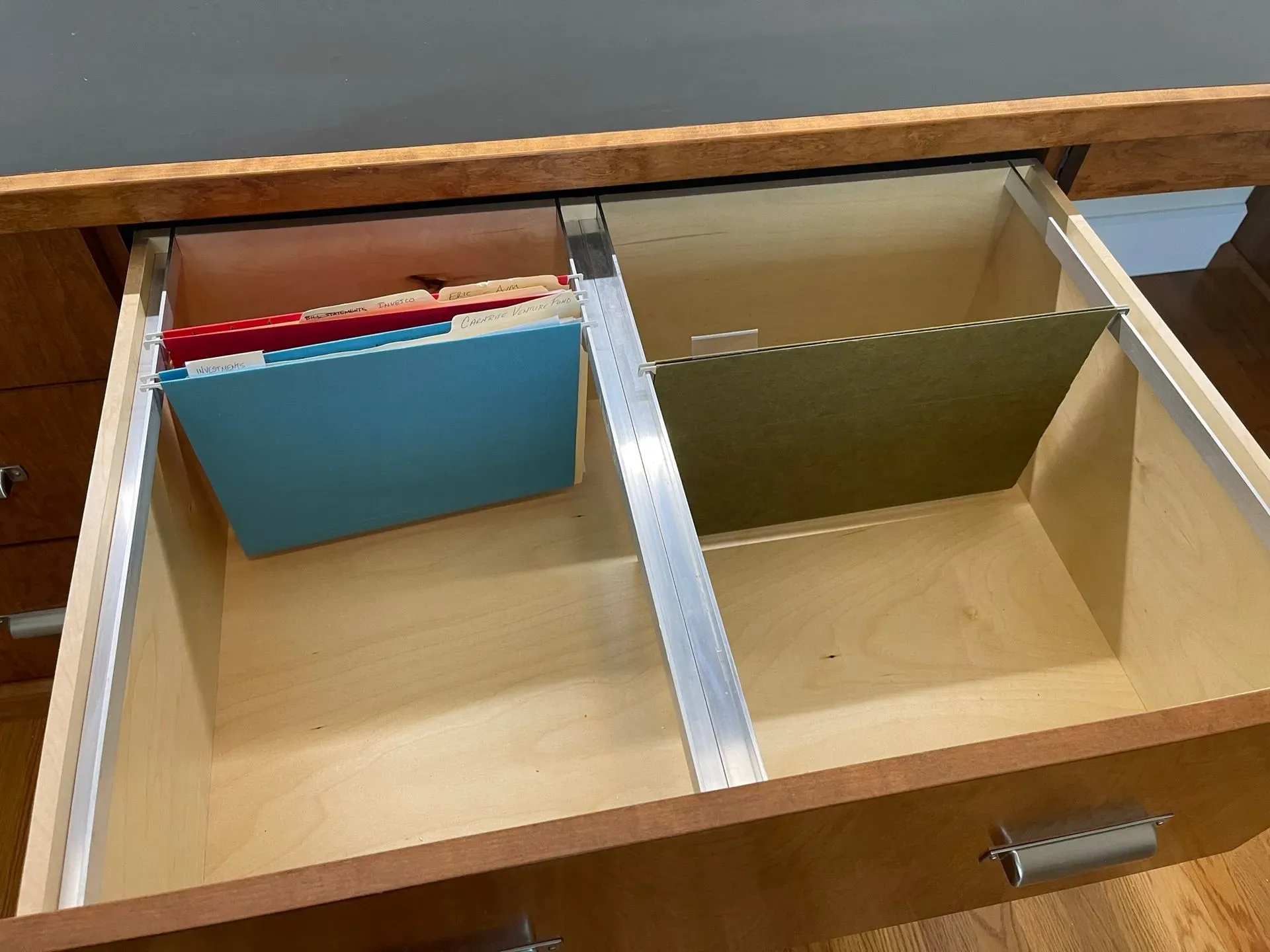 Open drawer with two wooden compartments, one holding blue and red folders.