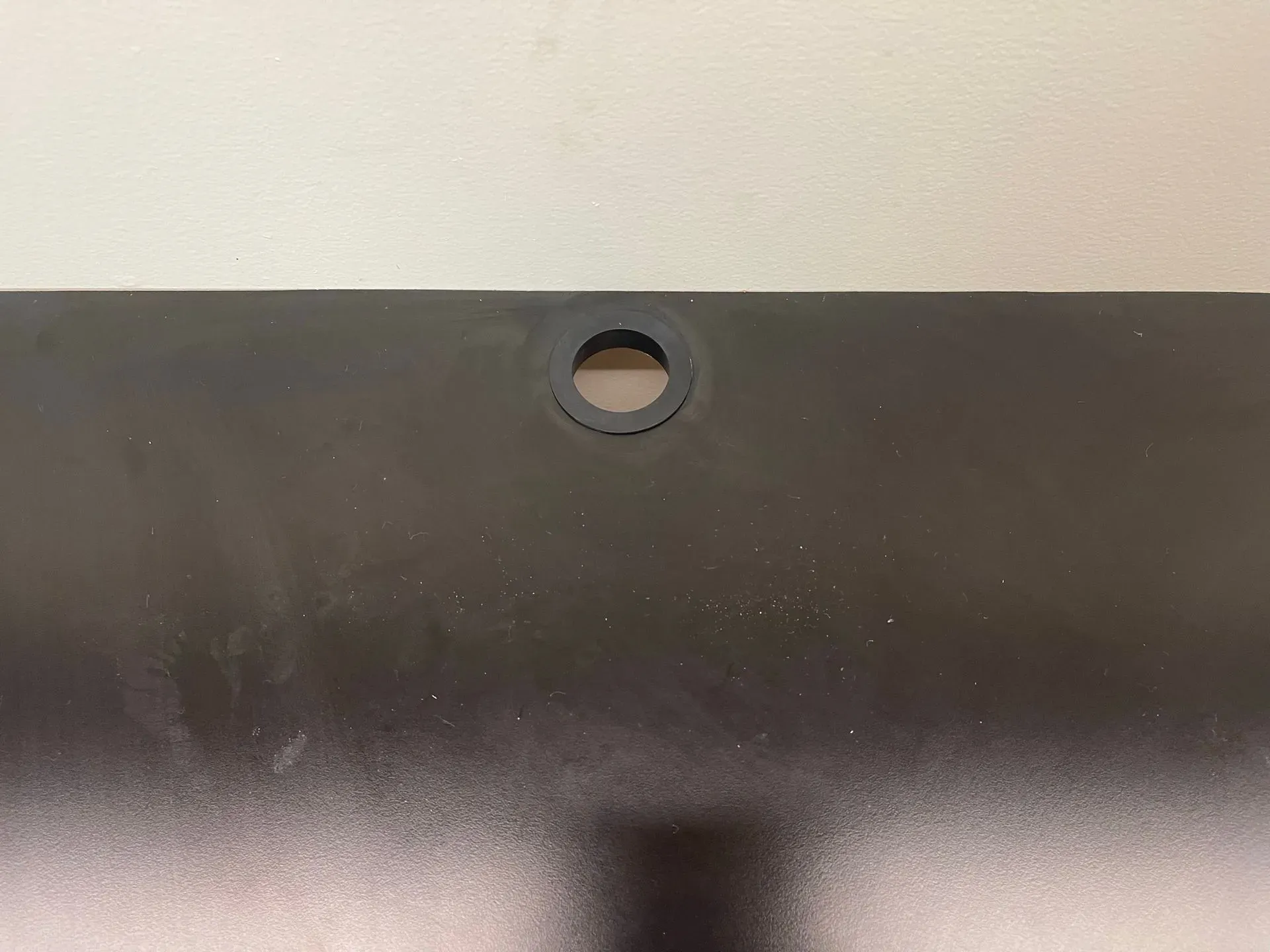 Black metal panel with a circular hole near the top center on a light wall background