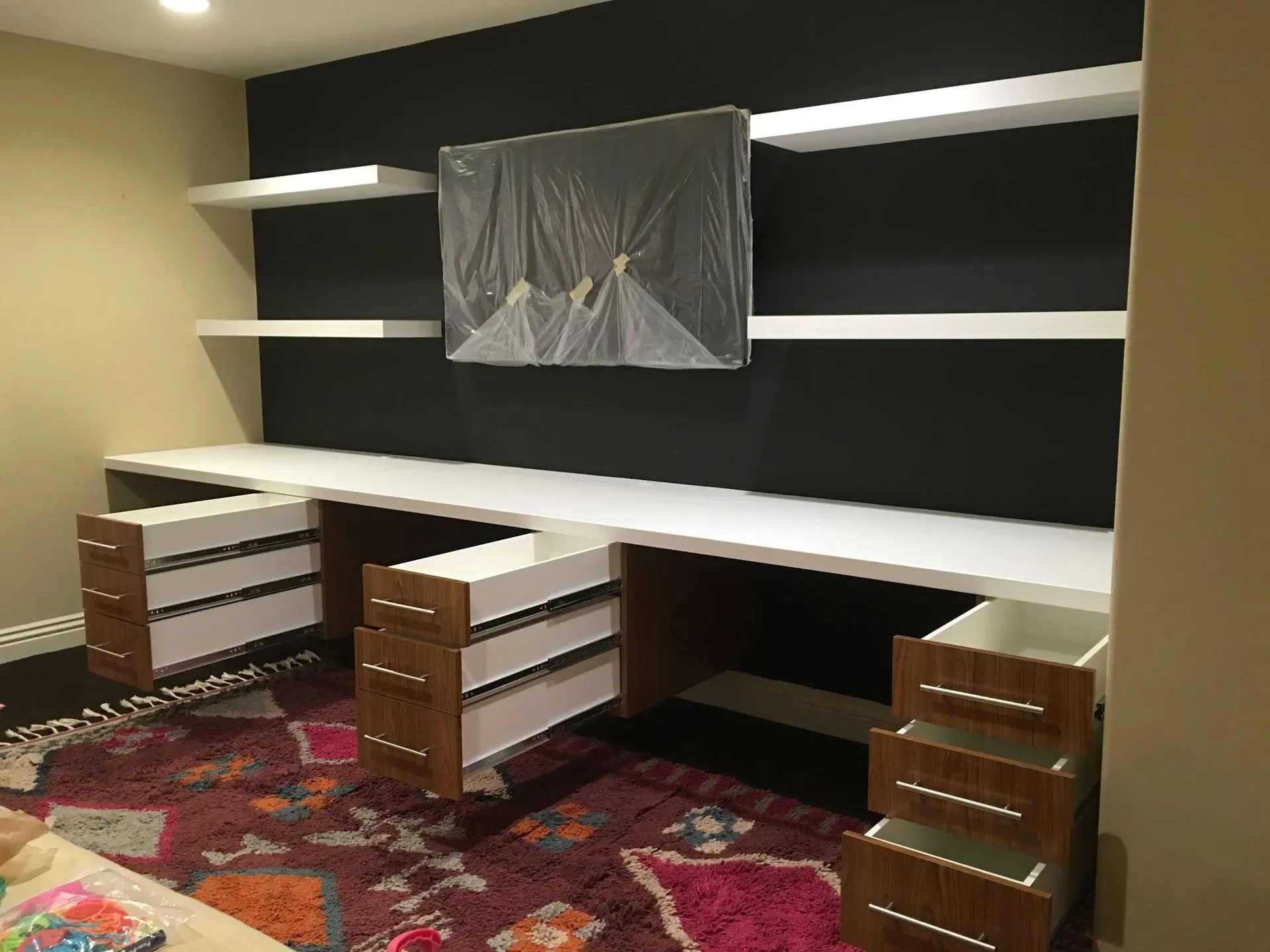 Built-in office with black wall, white shelves, twin desks, drawers, and a patterned rug