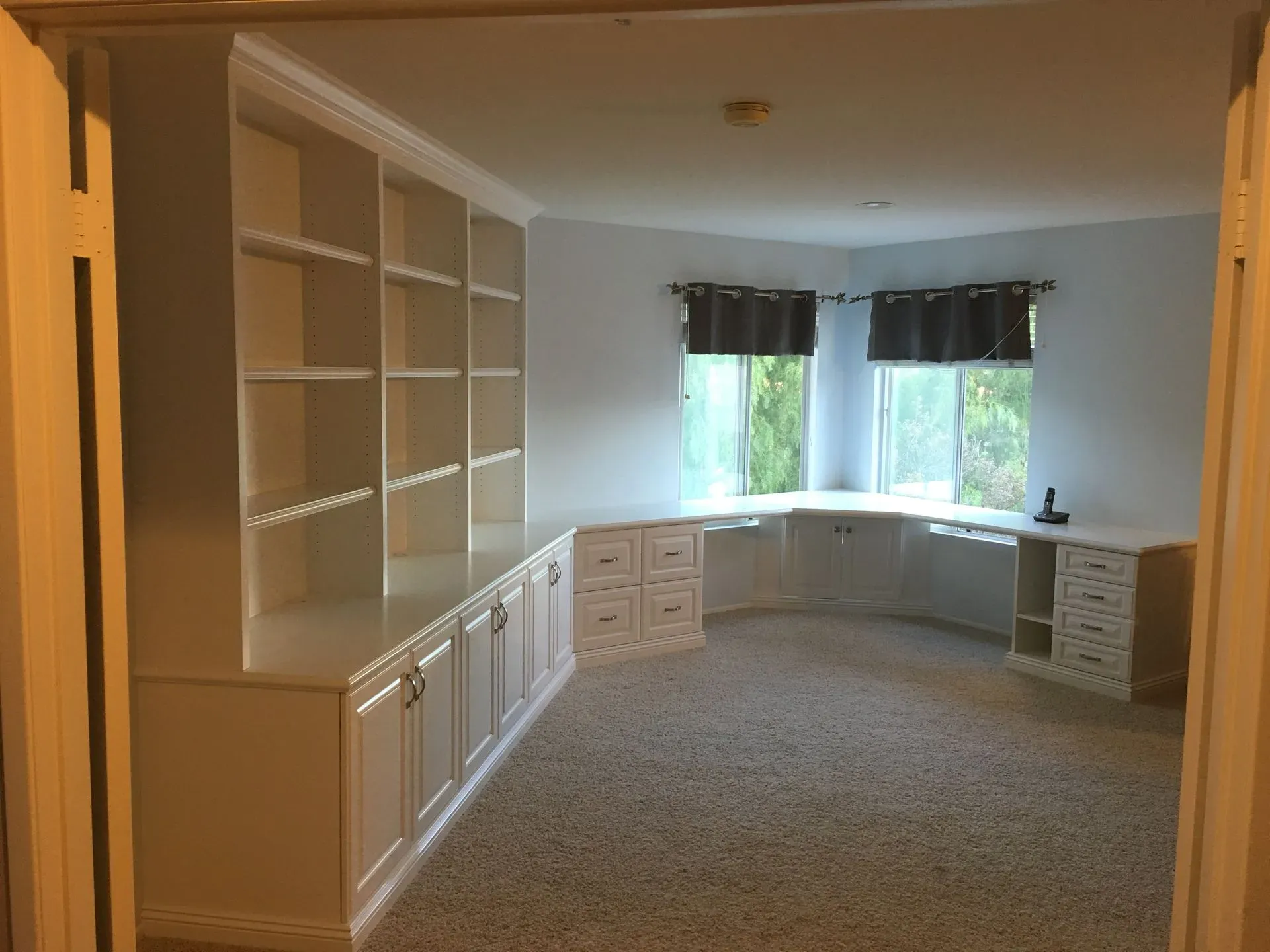 Built-in white cabinets and shelving in a carpeted room with windows and natural light
