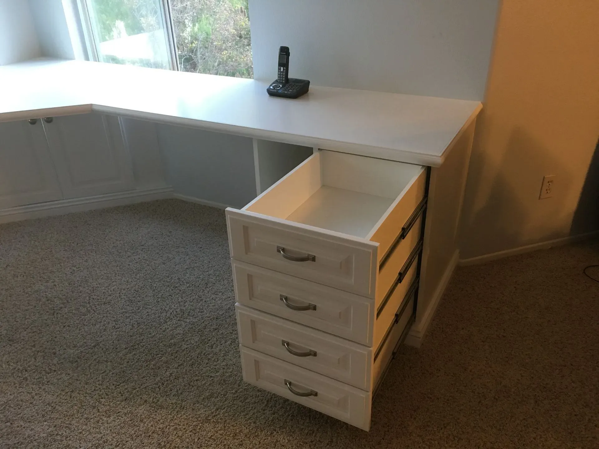 White corner desk with four drawers in a carpeted room, with a phone dock on top.