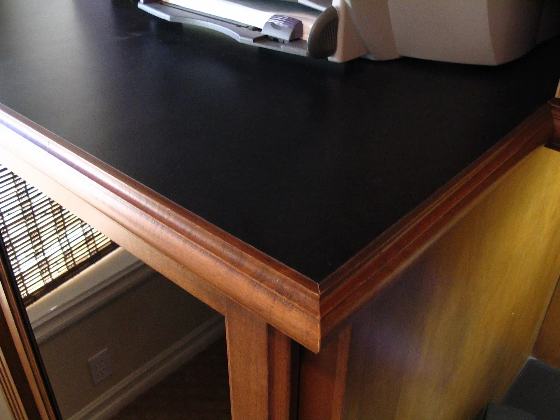 Black tabletop with wooden trim and a beige item on top, viewed at a corner indoors