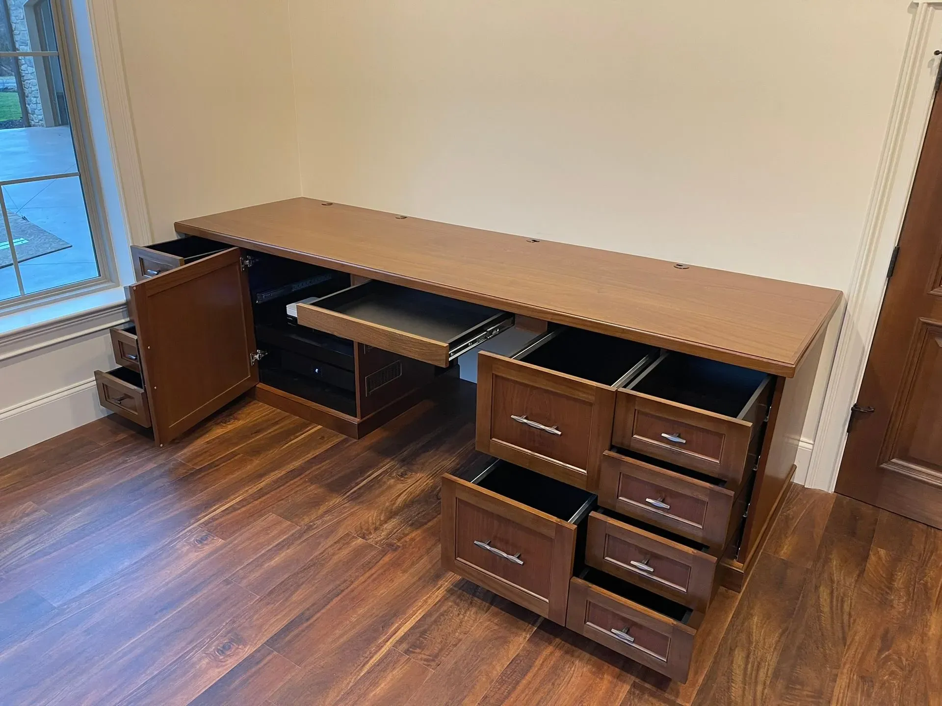 Wooden corner desk with multiple drawers and a pull-out keyboard tray in a room with wood flooring.