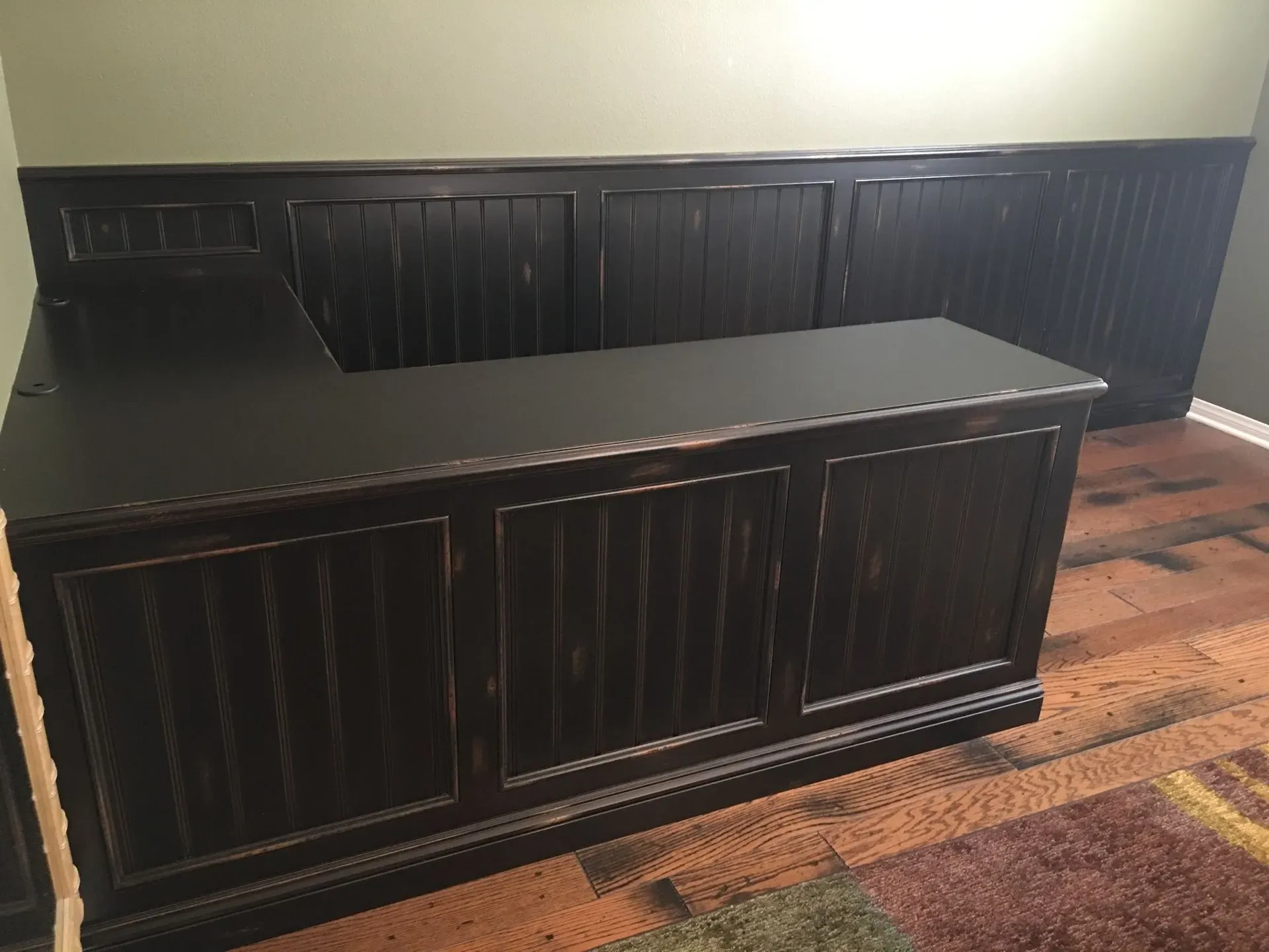 Black L-shaped reception desk with paneled fronts in an empty room with wood floors.