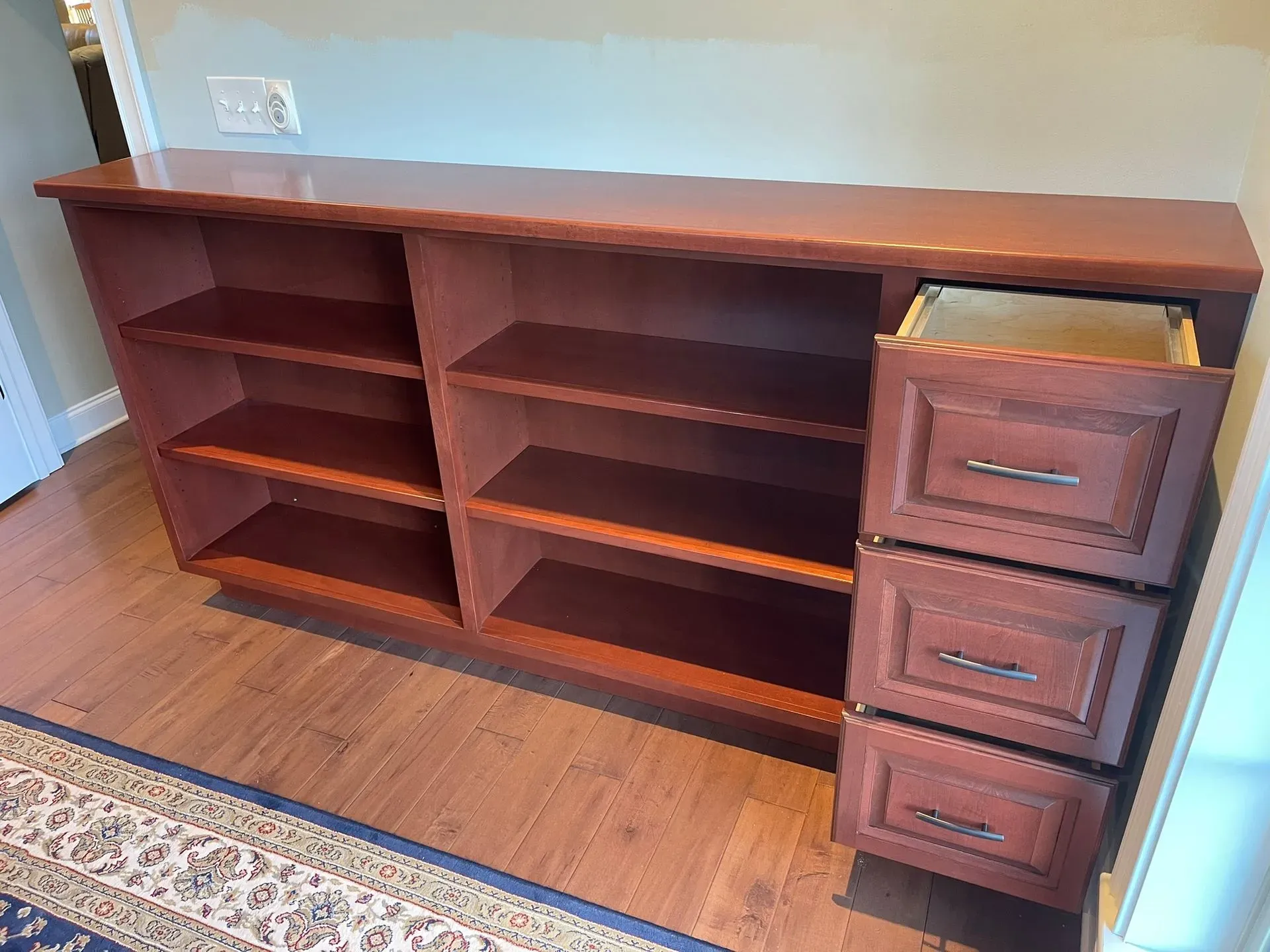 Wooden bookshelf with three drawers in a room with hardwood floors and a rug