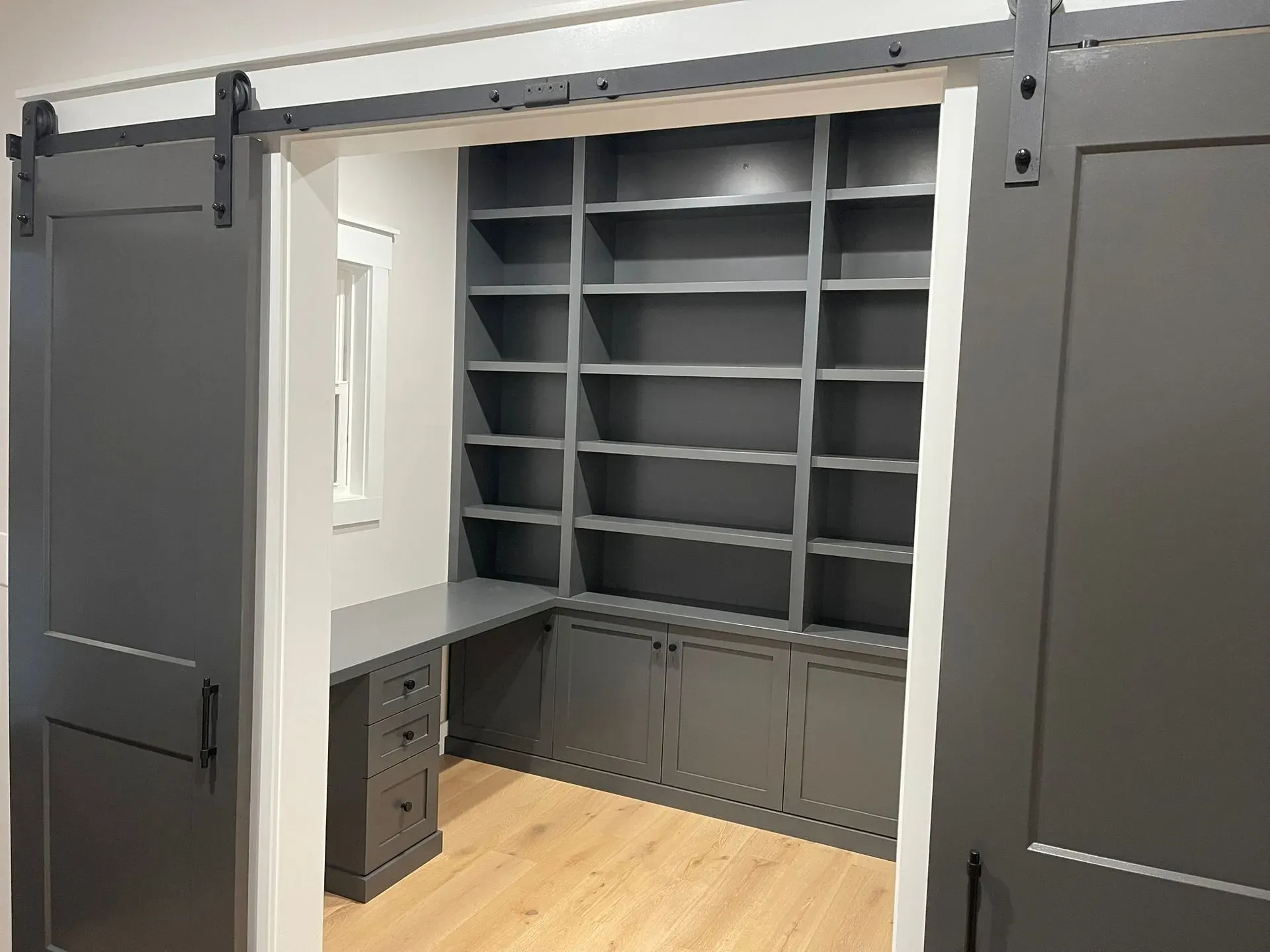 Gray built-in home office with desk, cabinets, and open shelving on a wood floor.