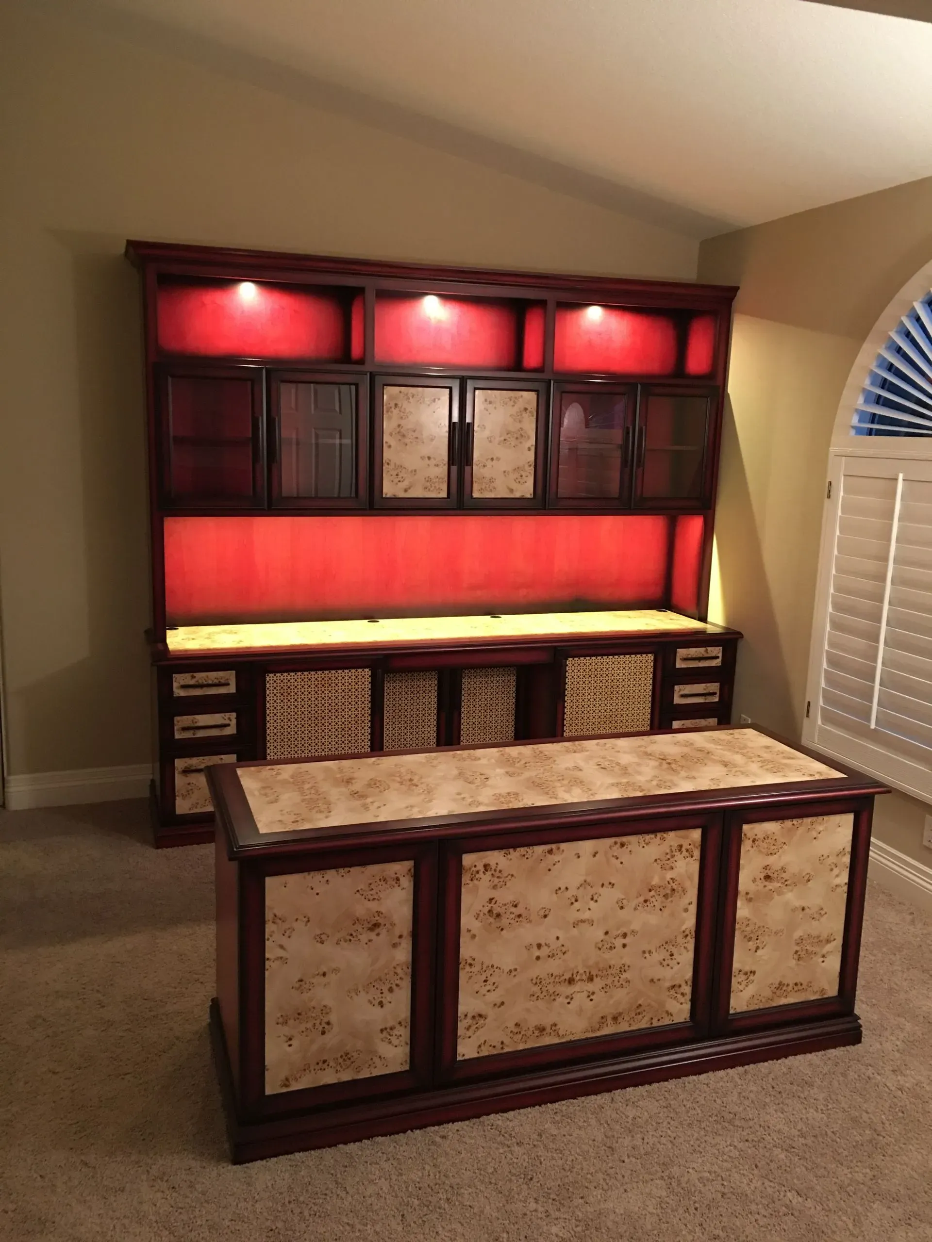Red-lit decorative display cabinet with patterned panels behind a matching wooden coffee table in a living room.