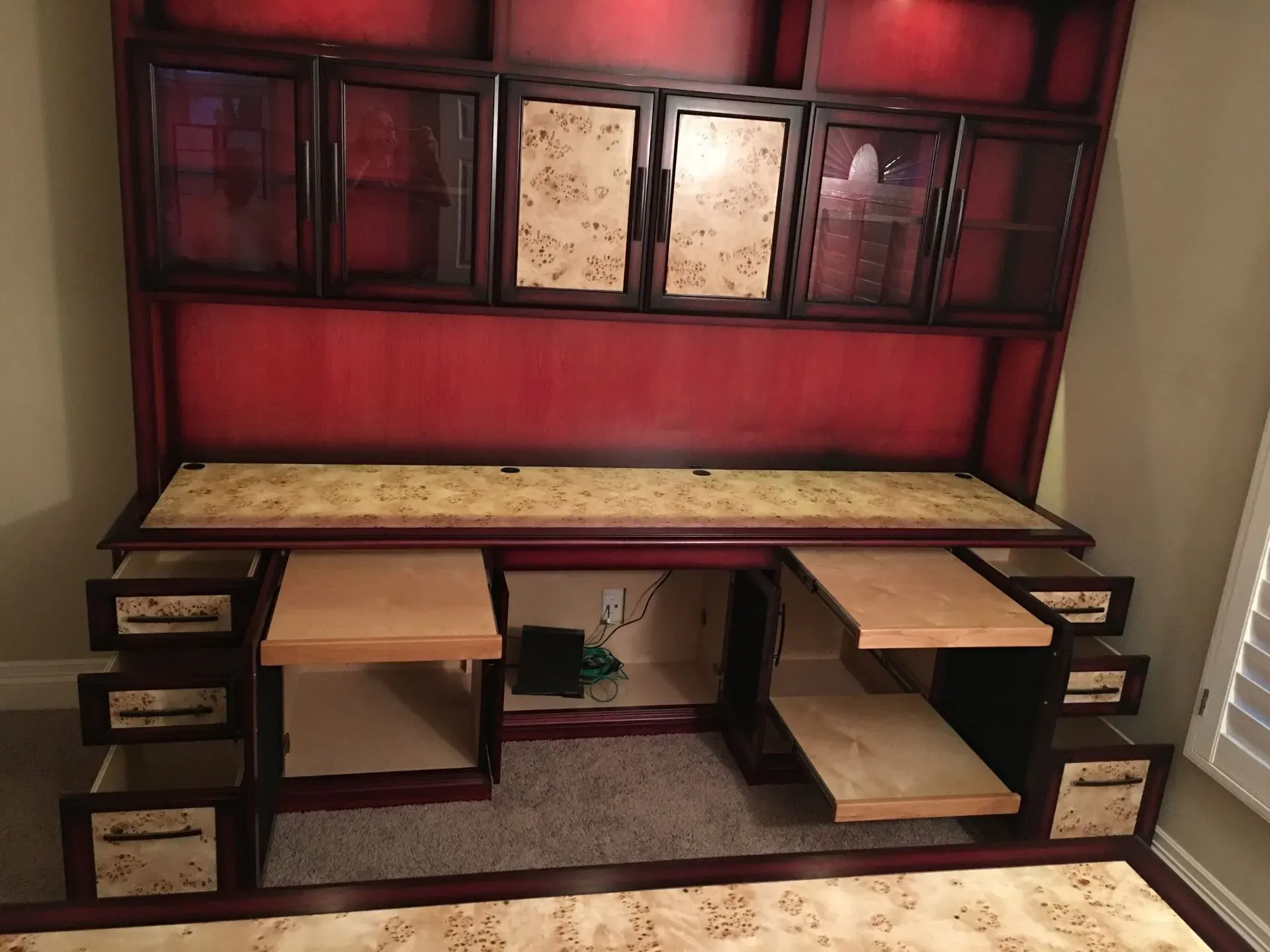 Red built-in desk with shelves and drawers, tan countertop, and a cushioned bench in a home office nook.