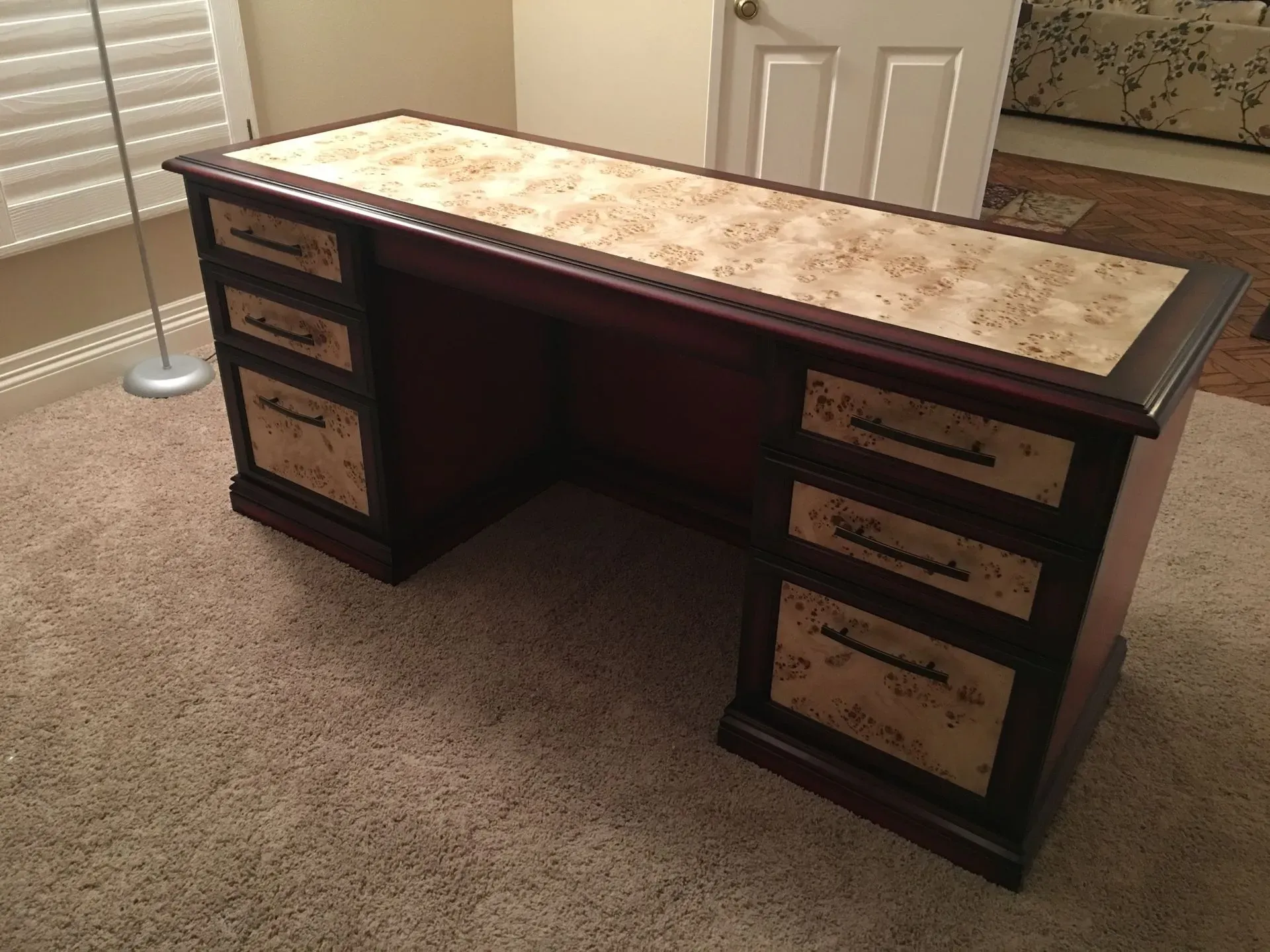 Dark wooden desk with drawers in a carpeted room beside a window and blinds
