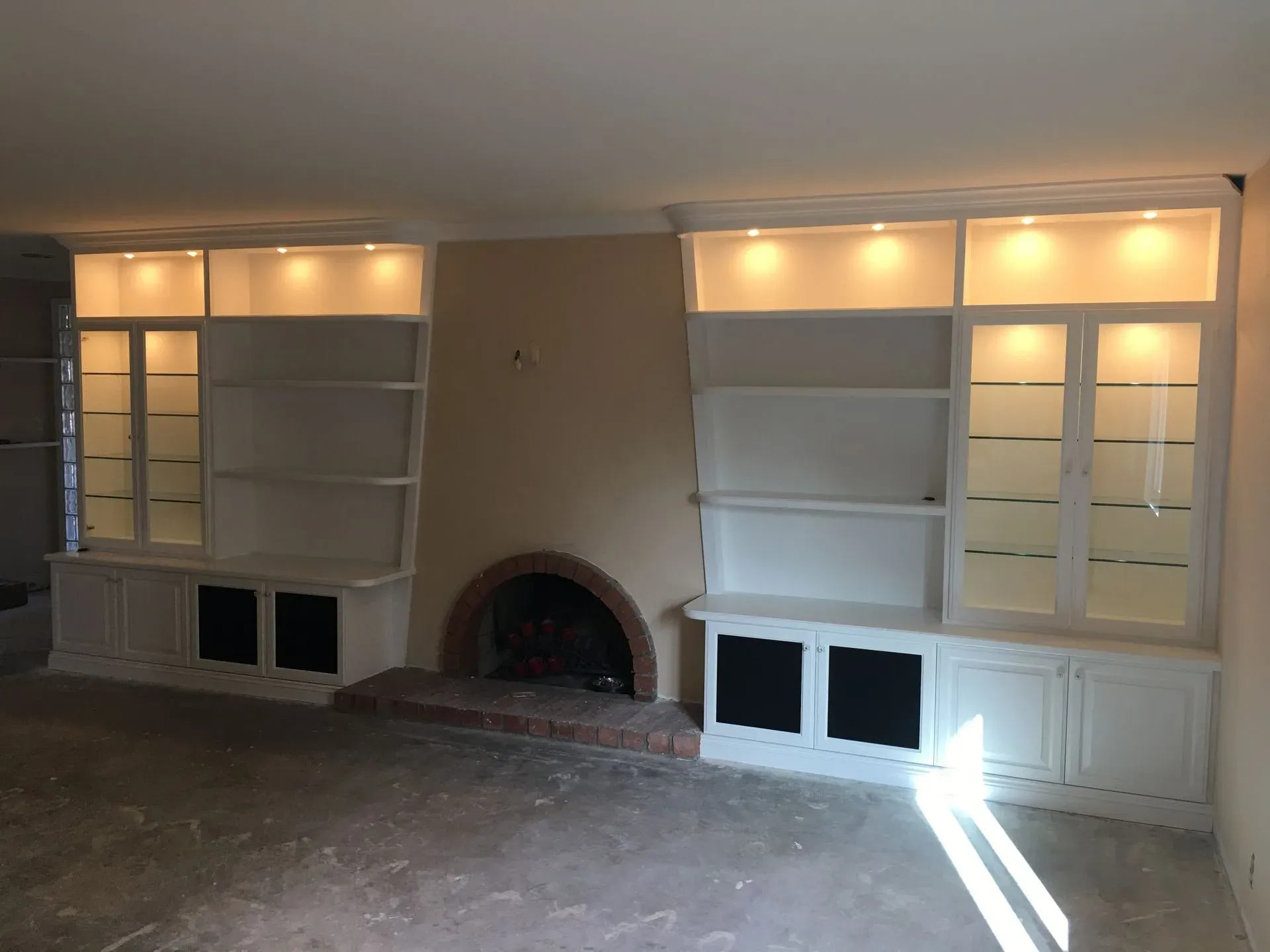 Built-in shelves and cabinets flanking a central fireplace in a living room with warm recessed lighting.