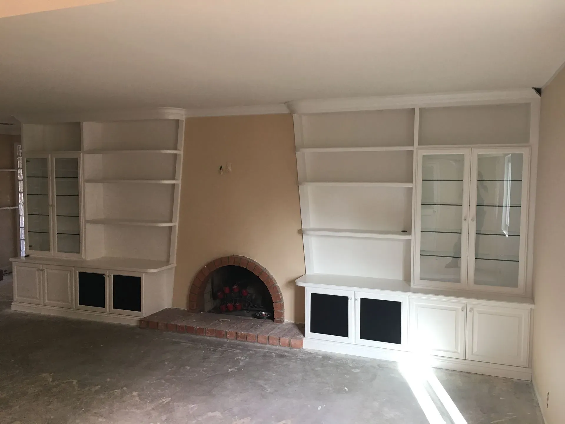 Living room with built-in white shelves and cabinets framing a central fireplace and beige chimney wall