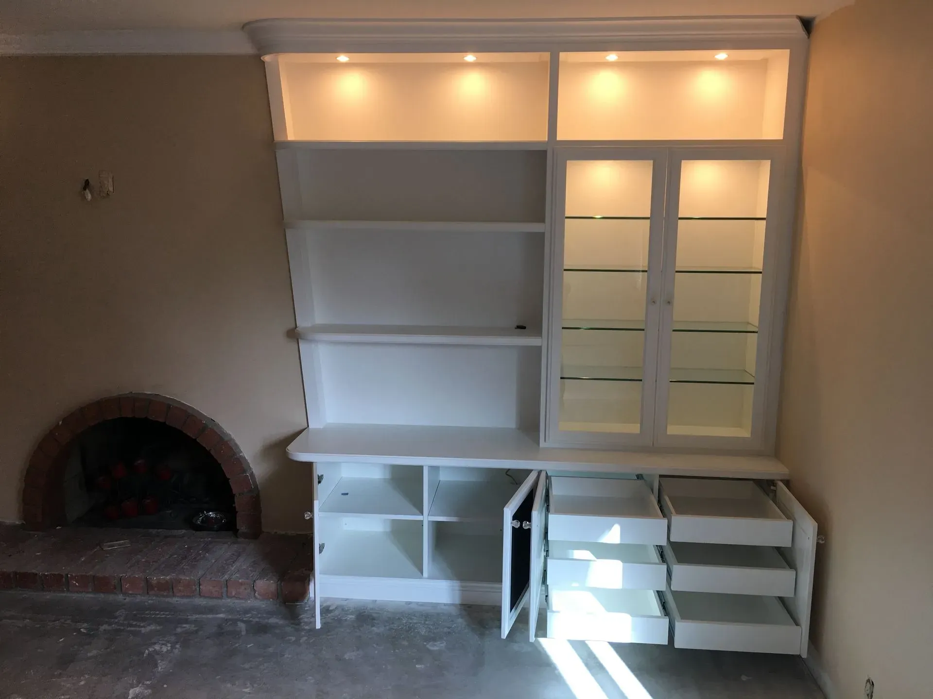 Built-in white shelving and cabinets beside a fireplace alcove in a beige room