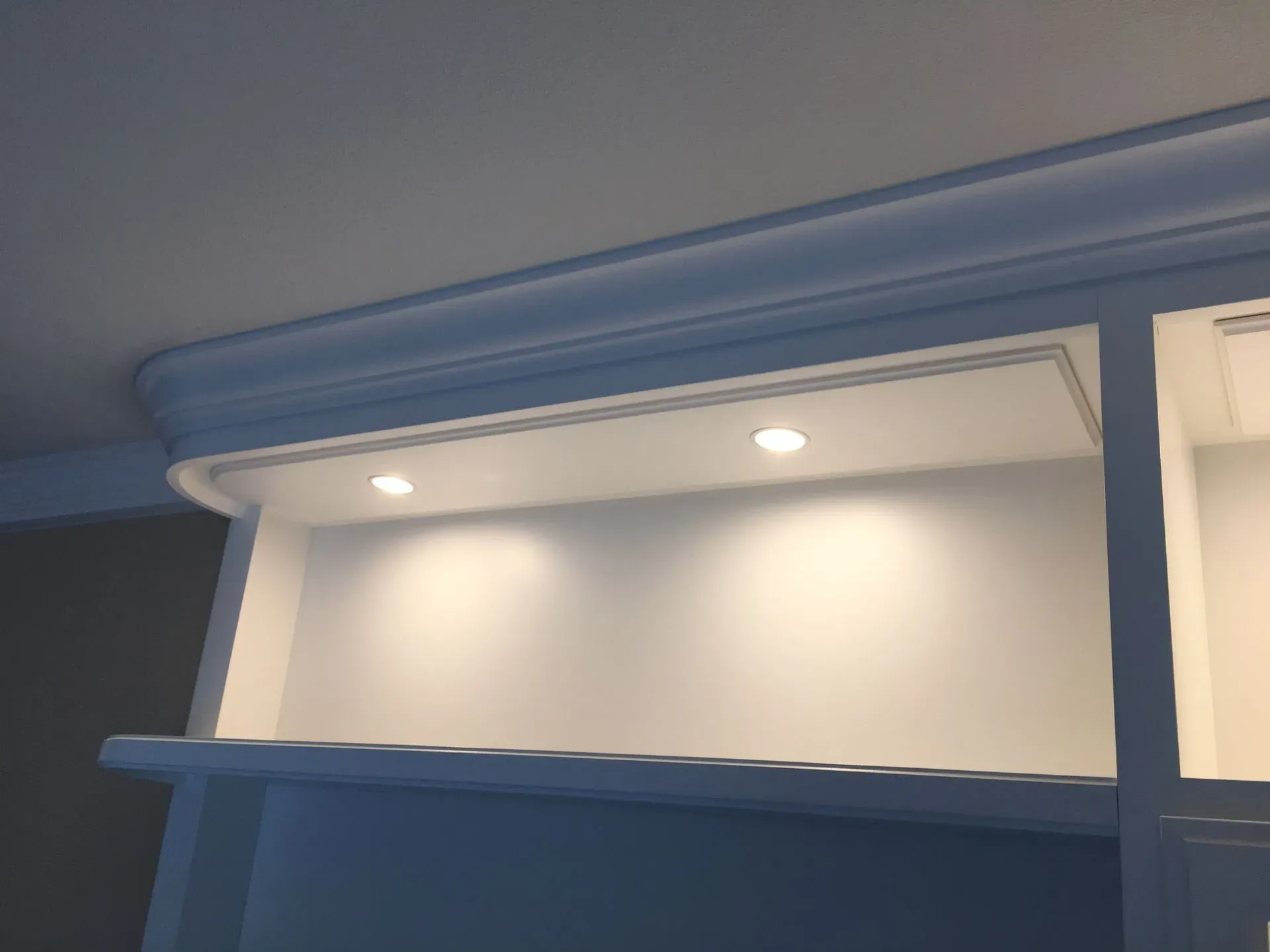 Blue cabinet with open shelf and recessed lights against a white wall and ceiling