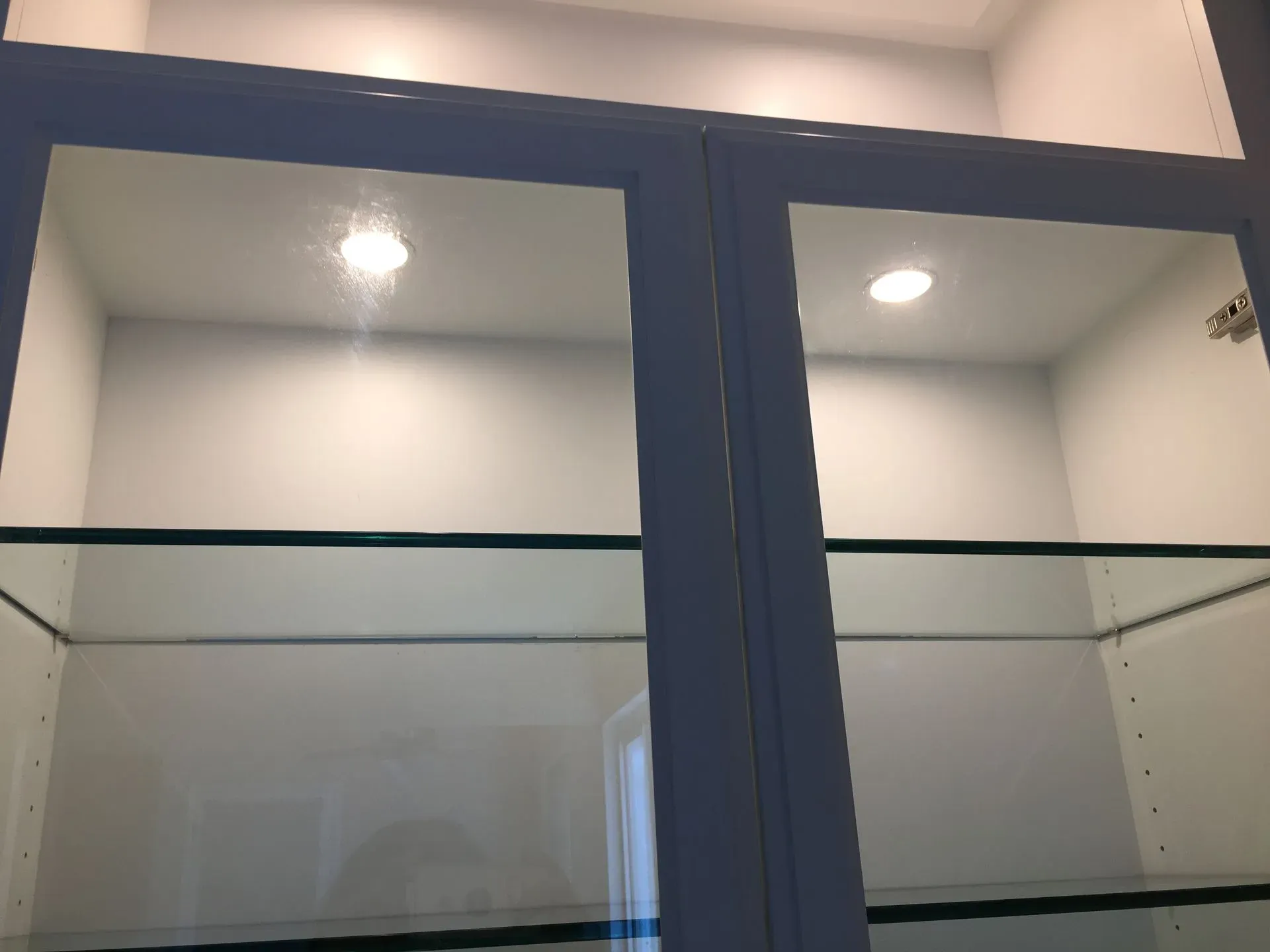 Blue-framed glass display cabinet with shelves, viewed indoors against a white wall.