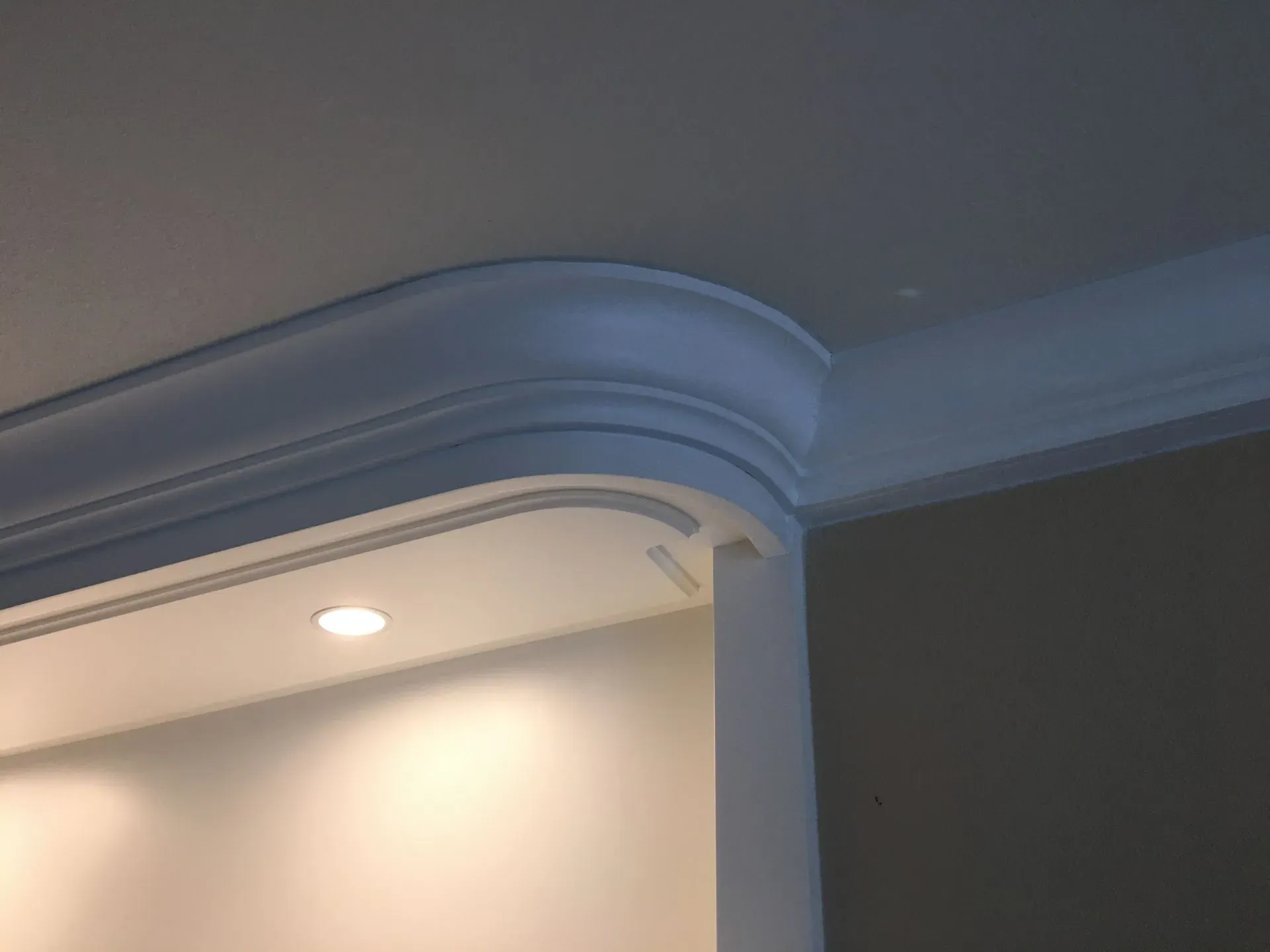 White crown molding with a curved corner over a lit ceiling recess in a modern interior