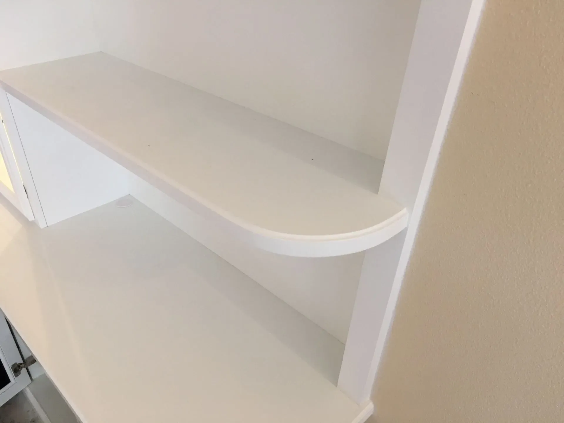 Built-in white shelving unit with curved front edge in a light beige room