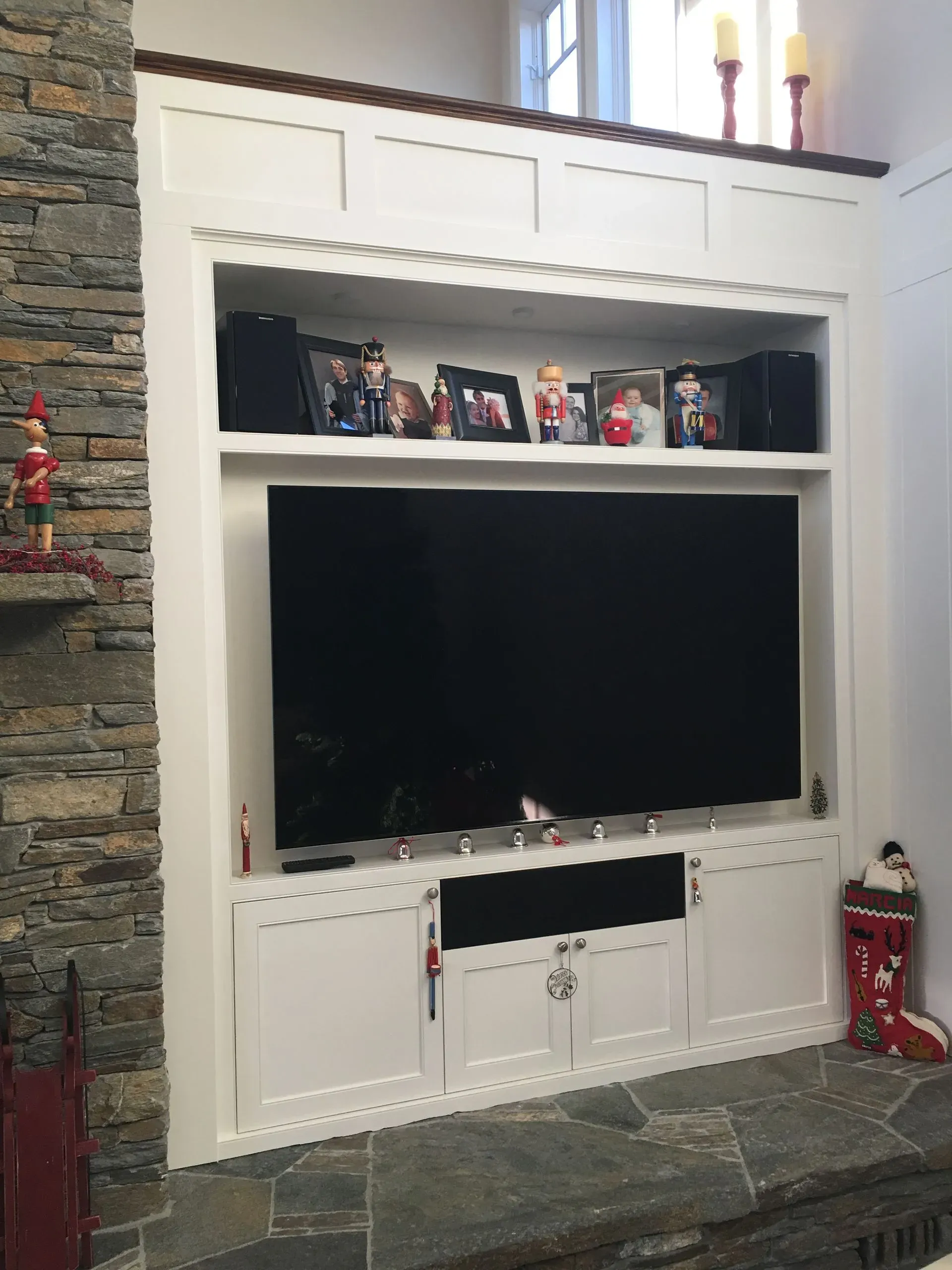 White built-in fireplace wall with a large TV, holiday figurines, candles, and stone hearth.