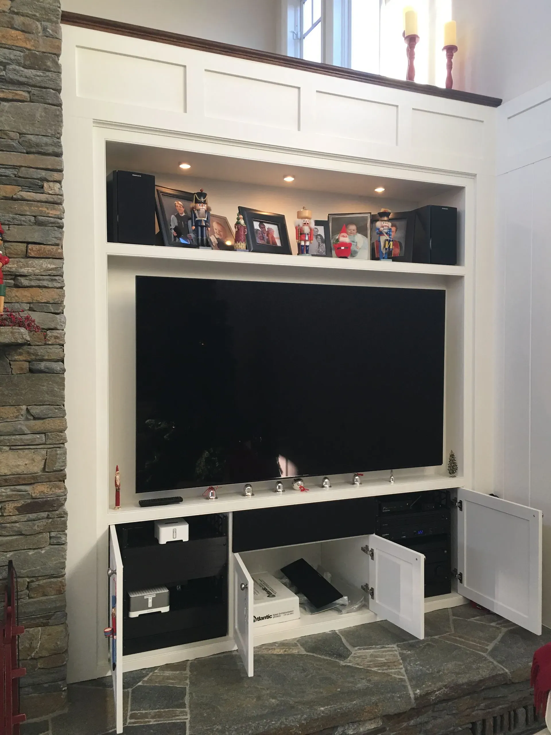 Built-in white media cabinet with a large TV, shelves of decor, and open lower storage doors