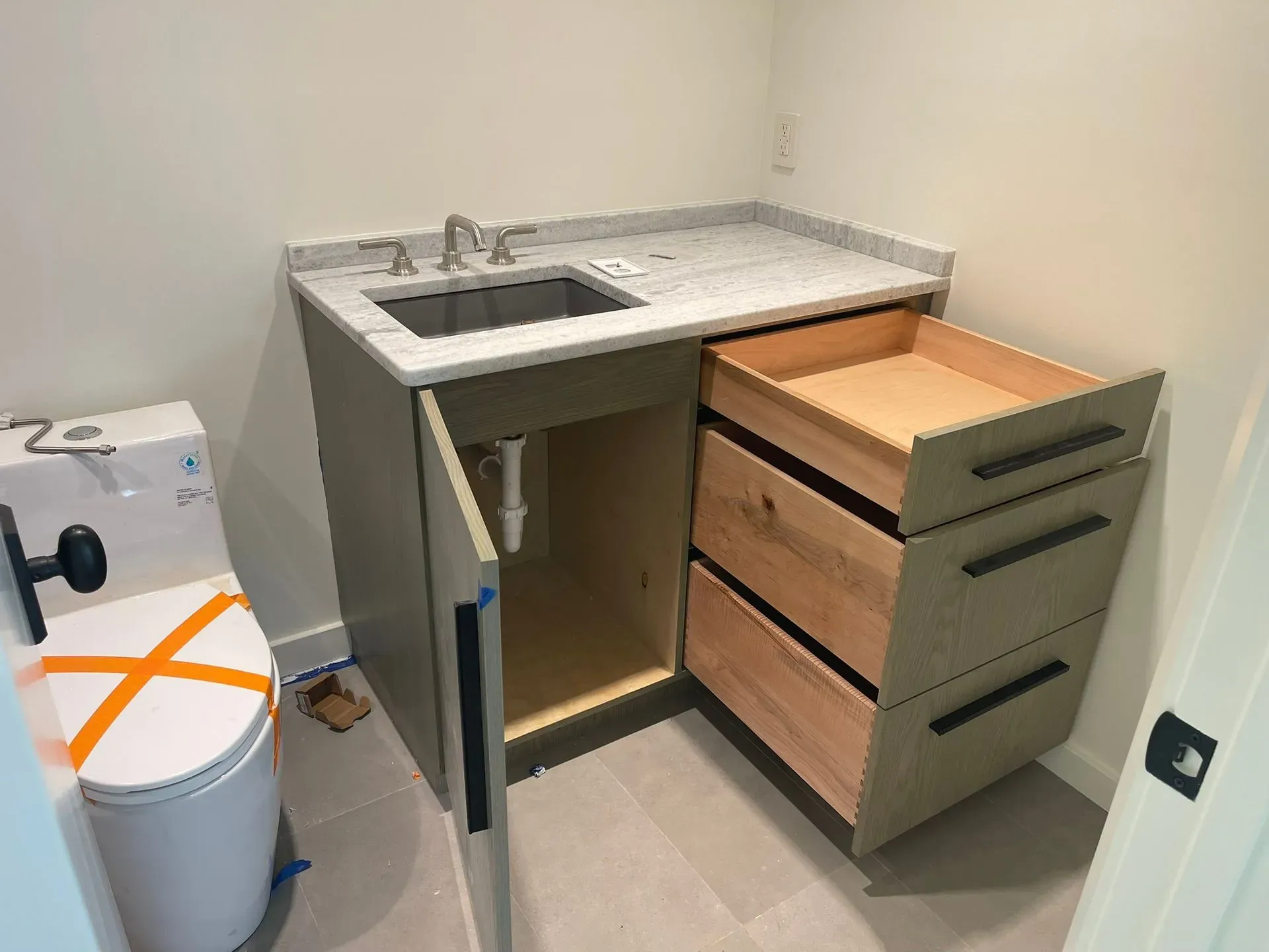Small bathroom vanity with sink, open cabinet, and drawers beside a toilet.
