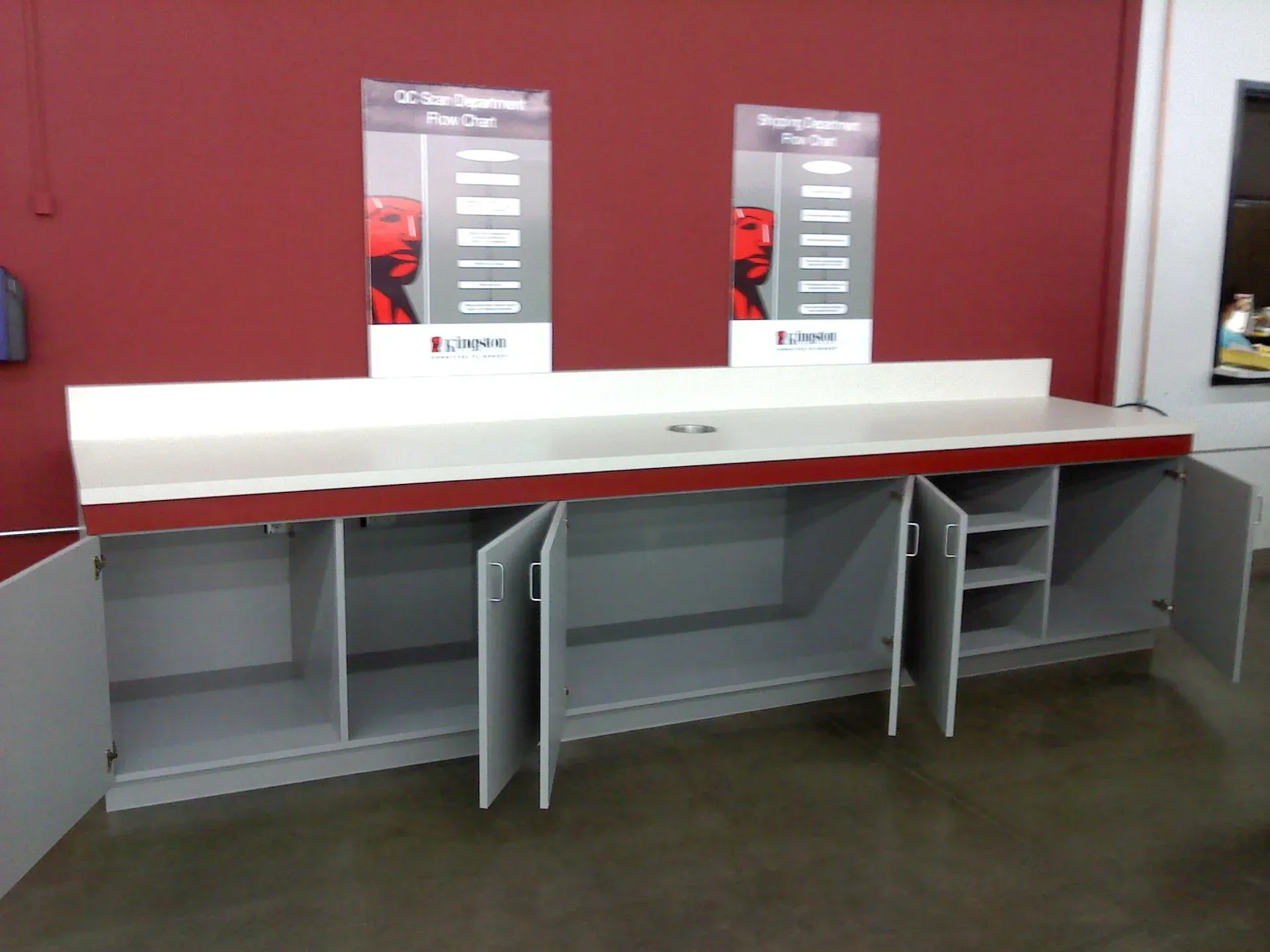 Long white reception counter with gray cubbies against a red wall in an empty room