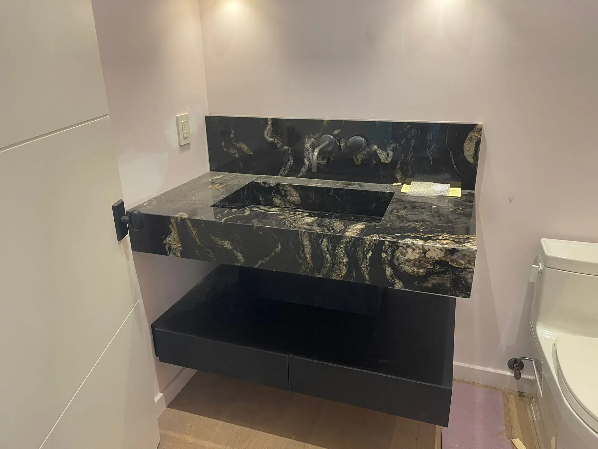 Modern bathroom vanity with black marble sink and open shelf under warm wall lights