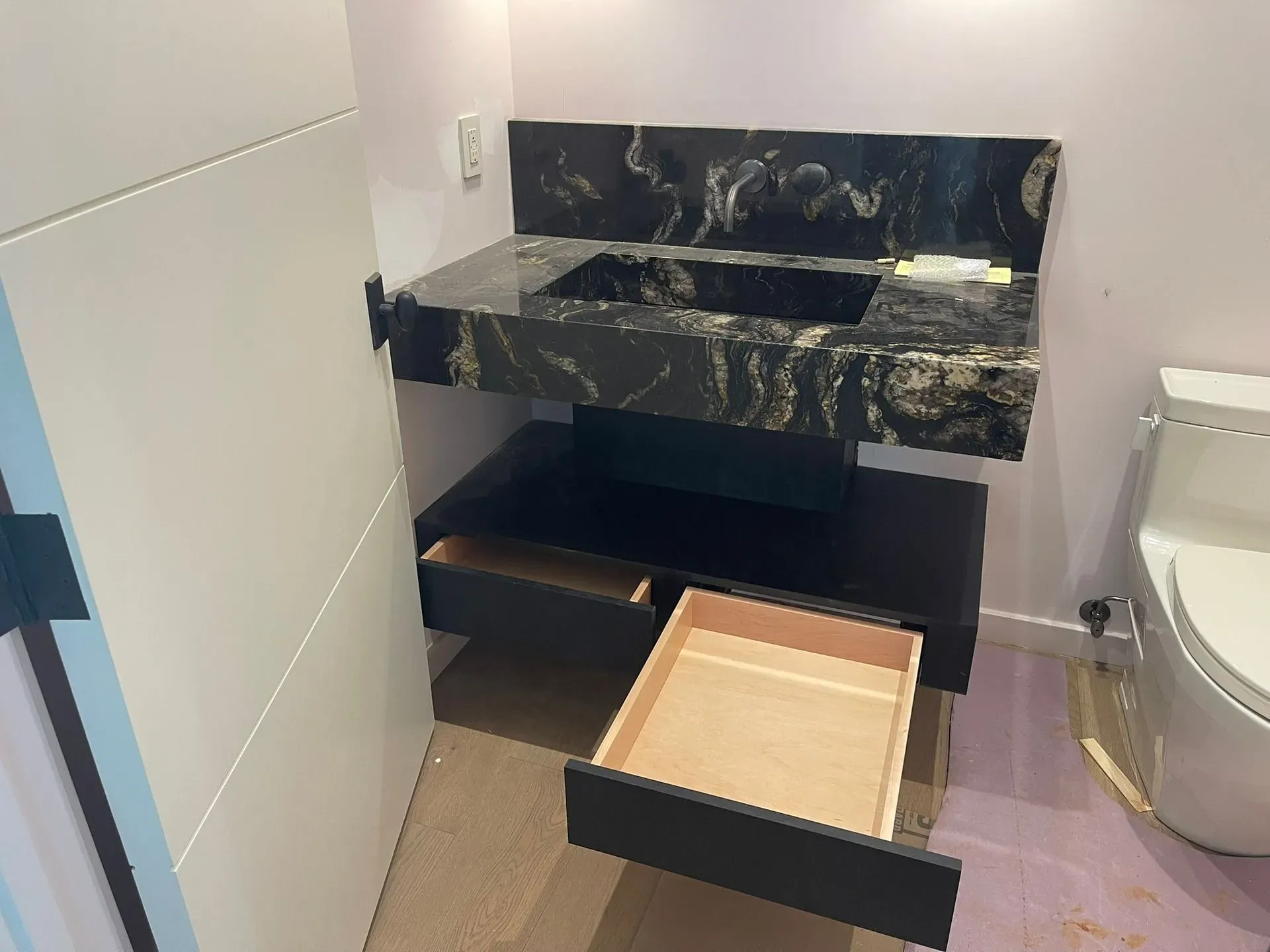 Bathroom vanity with a black marble countertop and an open drawer on the floor partially pulled out.