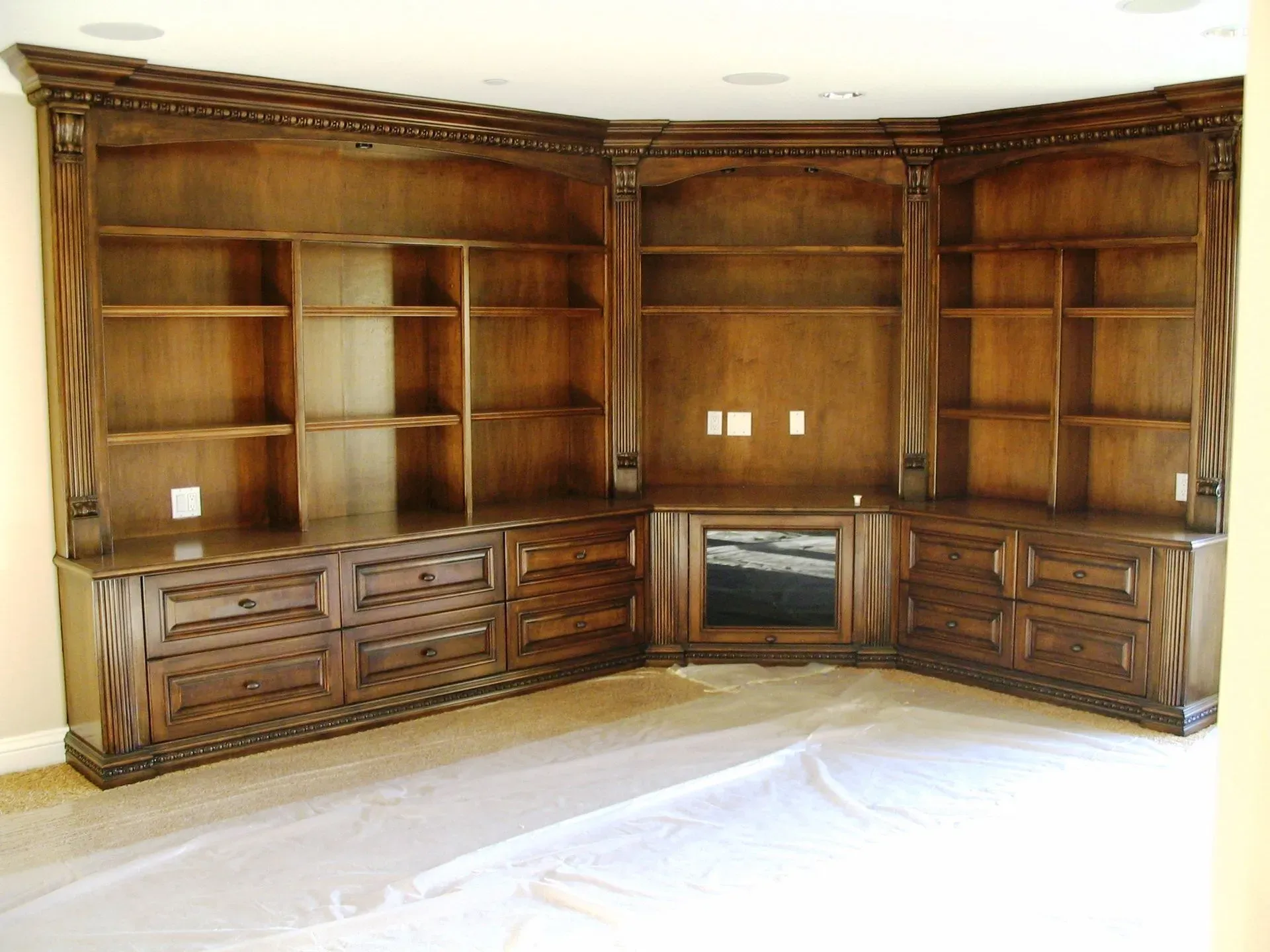 Built-in wooden corner entertainment center with shelves and cabinets in a beige room