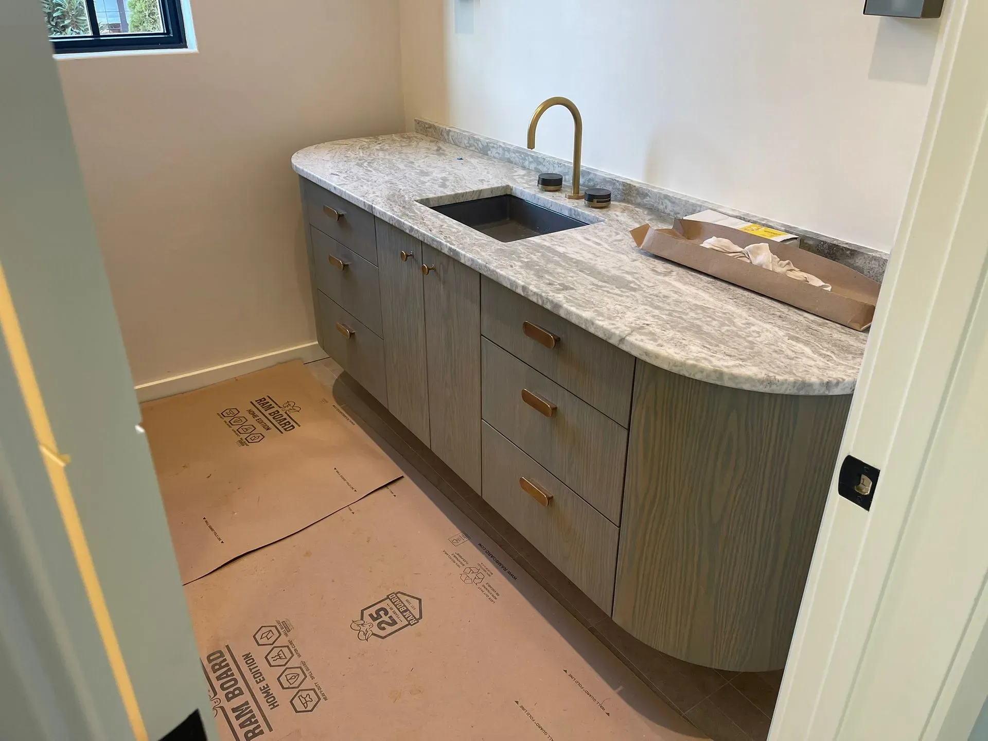 Unfinished bathroom vanity with sink and faucet, surrounded by protective floor covering.