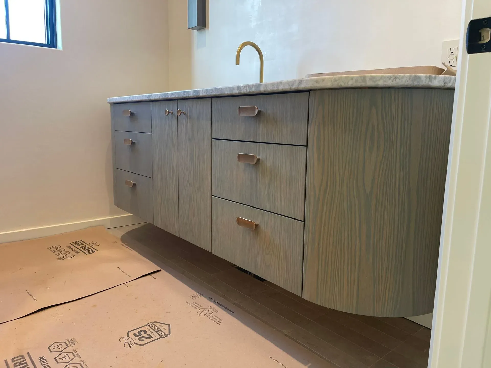 Modern bathroom vanity with wood cabinets, white countertop, and sink in a partially finished room.