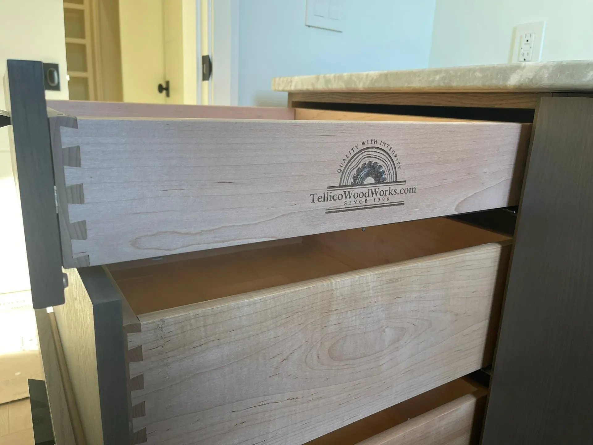 Open dresser drawers with a branded wood front in a bedroom.