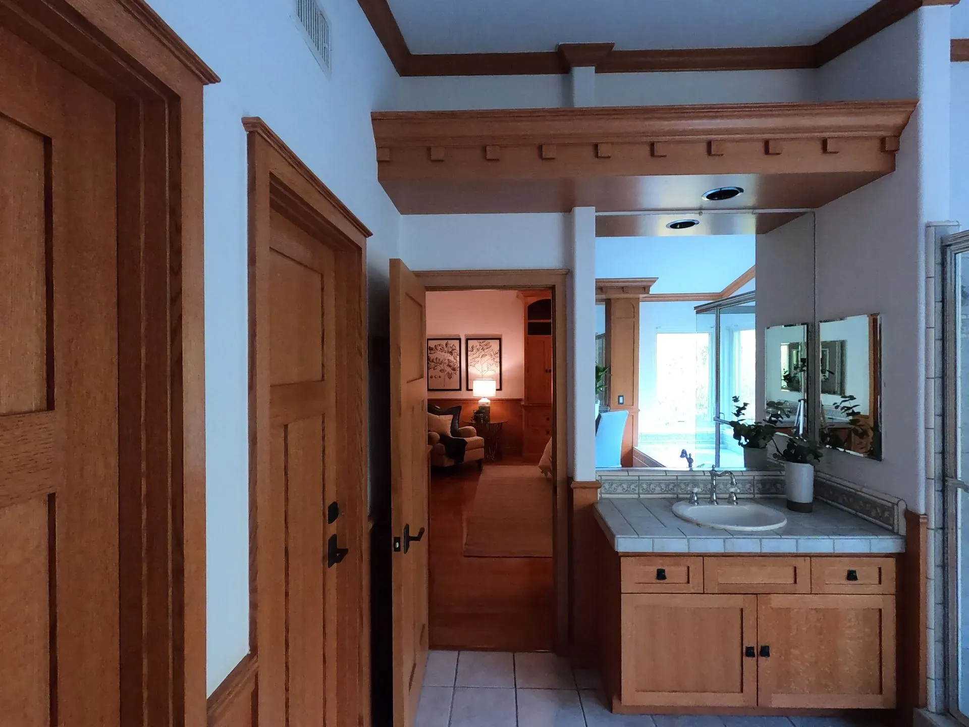 Bathroom vanity and doorway leading to a softly lit bedroom, with wood trim and a sink on the right.