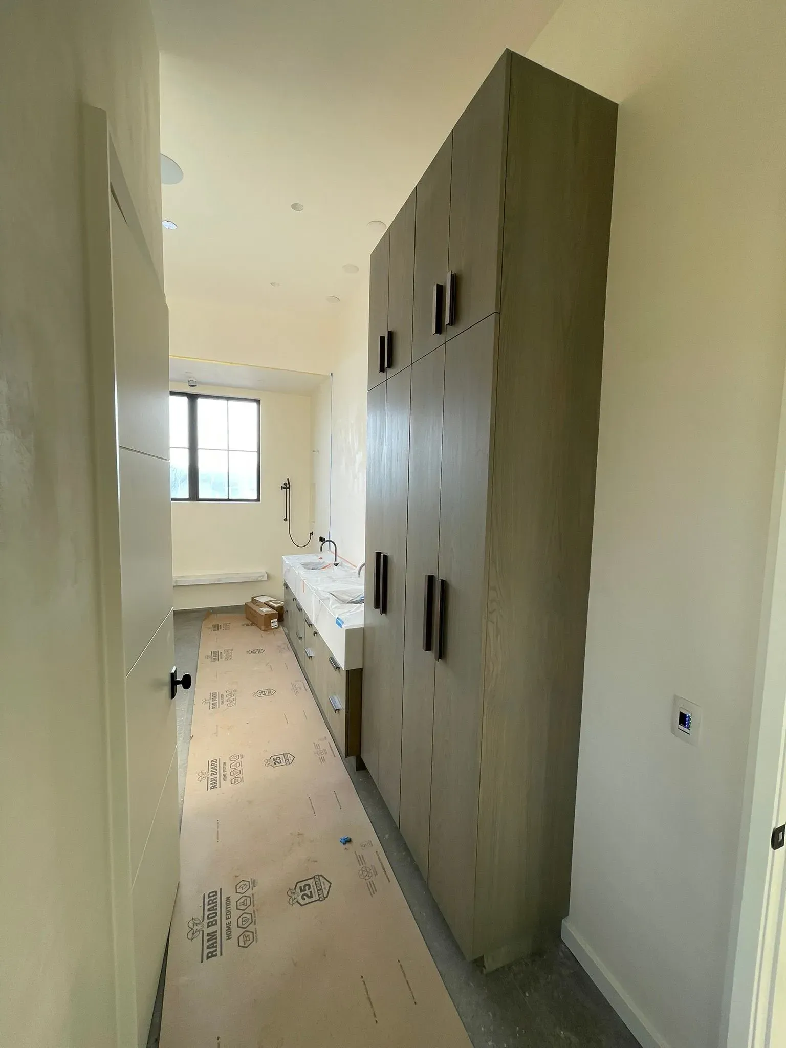 Narrow unfinished hallway with built-in cabinets, white walls, and a window at the end.