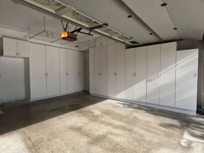 Empty garage with white storage cabinets along the wall and sunlight on the concrete floor
