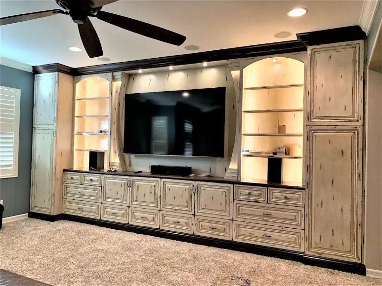 Built-in entertainment center with TV, white cabinets, and recessed lighting in a carpeted living room