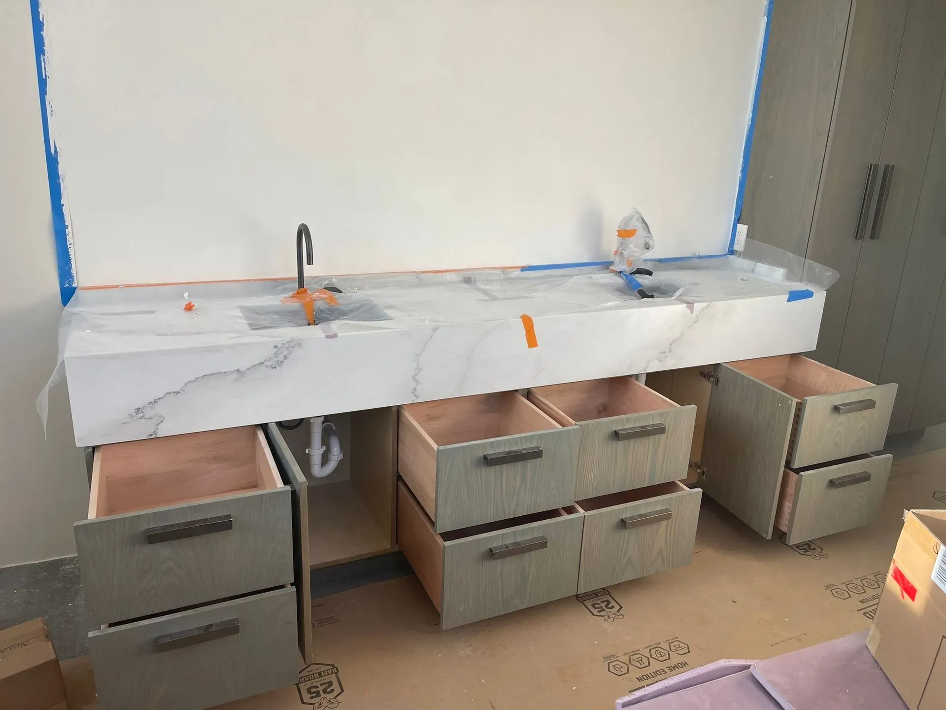 Bathroom vanity under construction with marble-look countertop, two sinks, and open drawers and cabinets