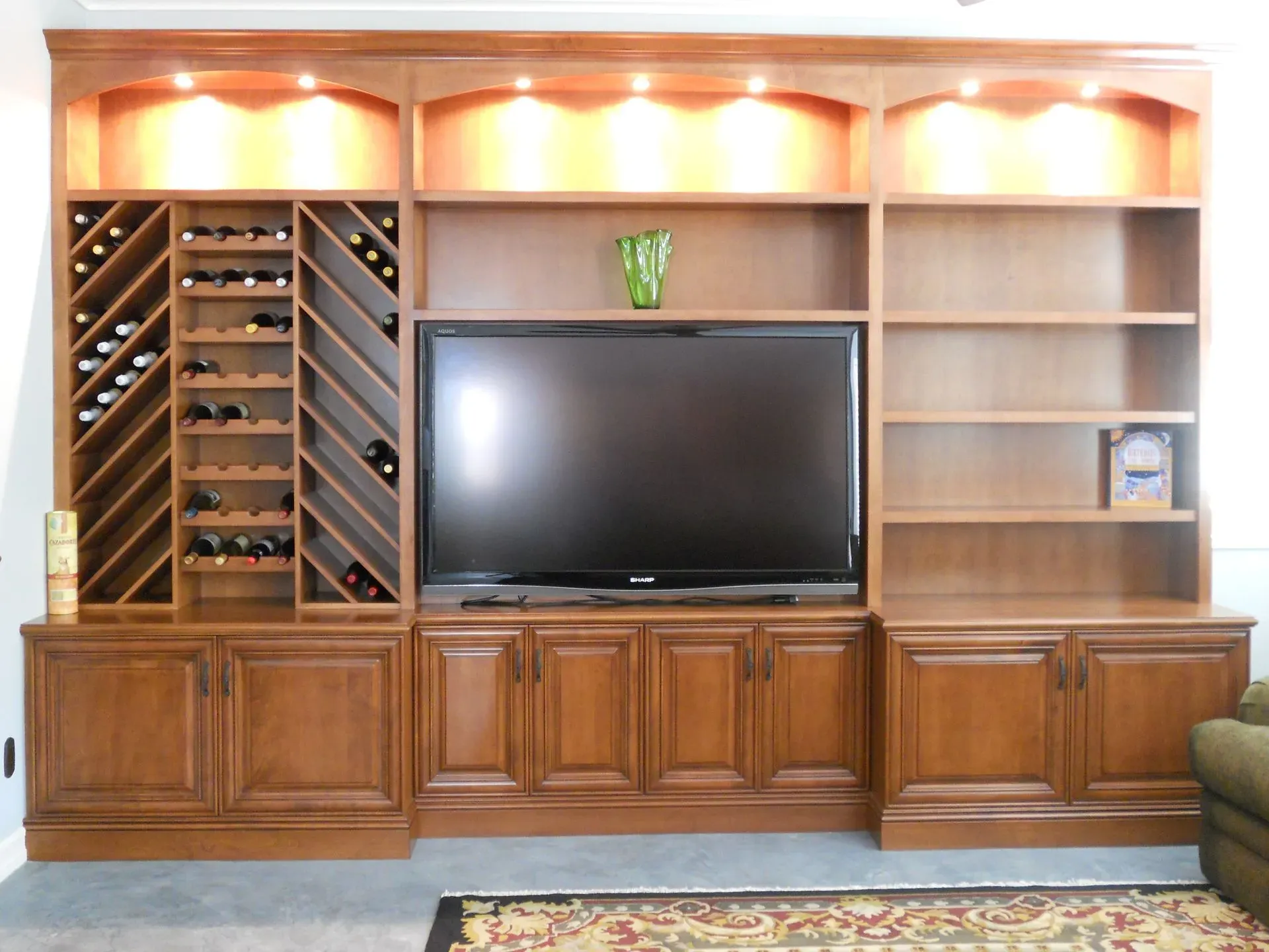 Wooden living room wall unit with wine racks, TV, shelves, and warm recessed lighting