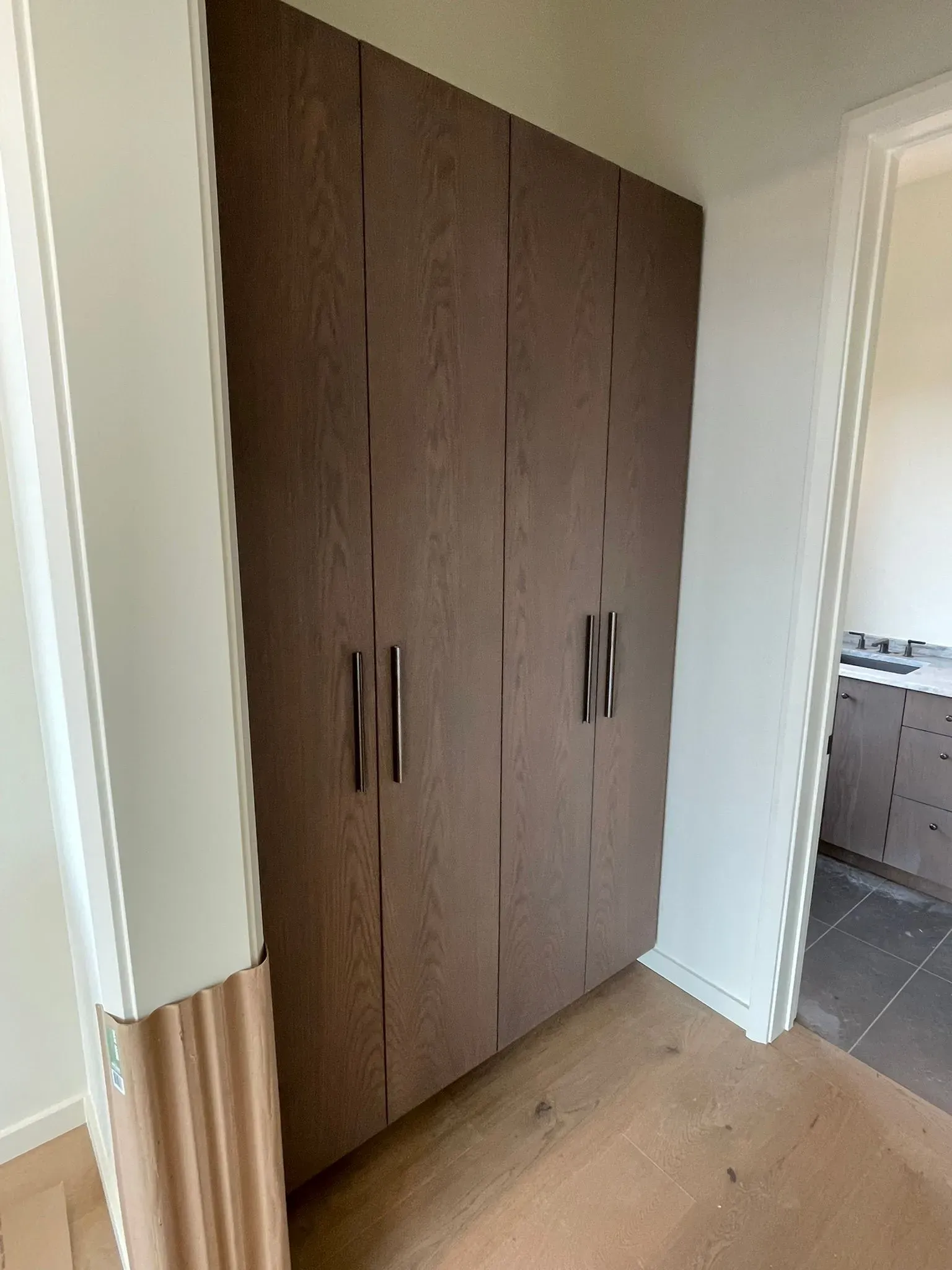 Built-in brown wardrobe in a small hallway beside a doorway and tiled room