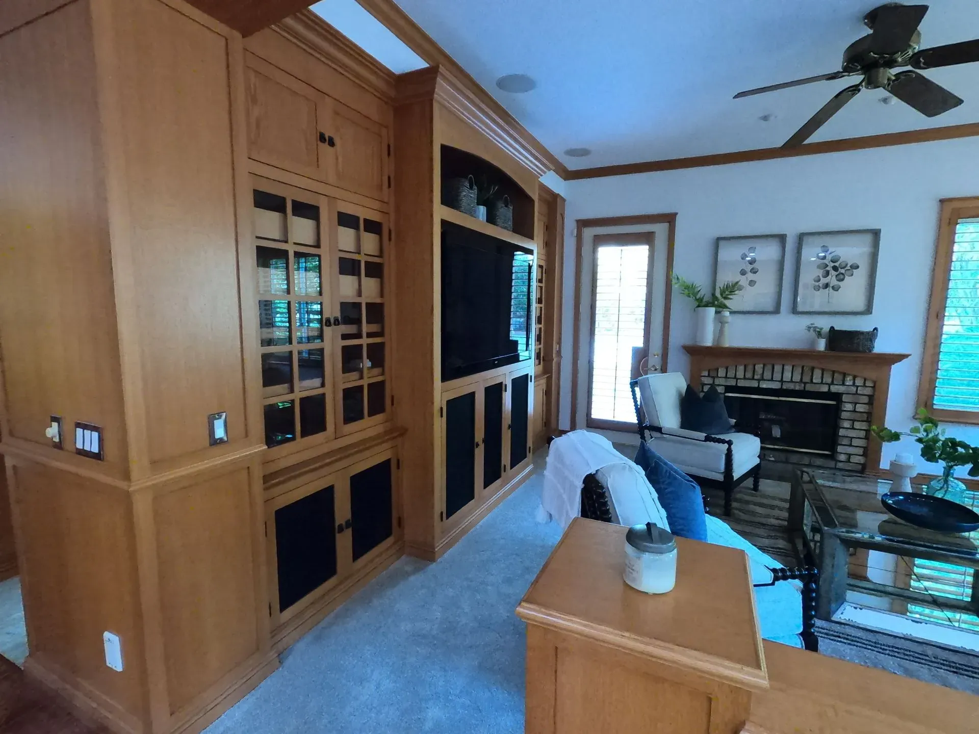Living room with wood built-ins, fireplace, blue sofa, glass coffee table, and ceiling fan