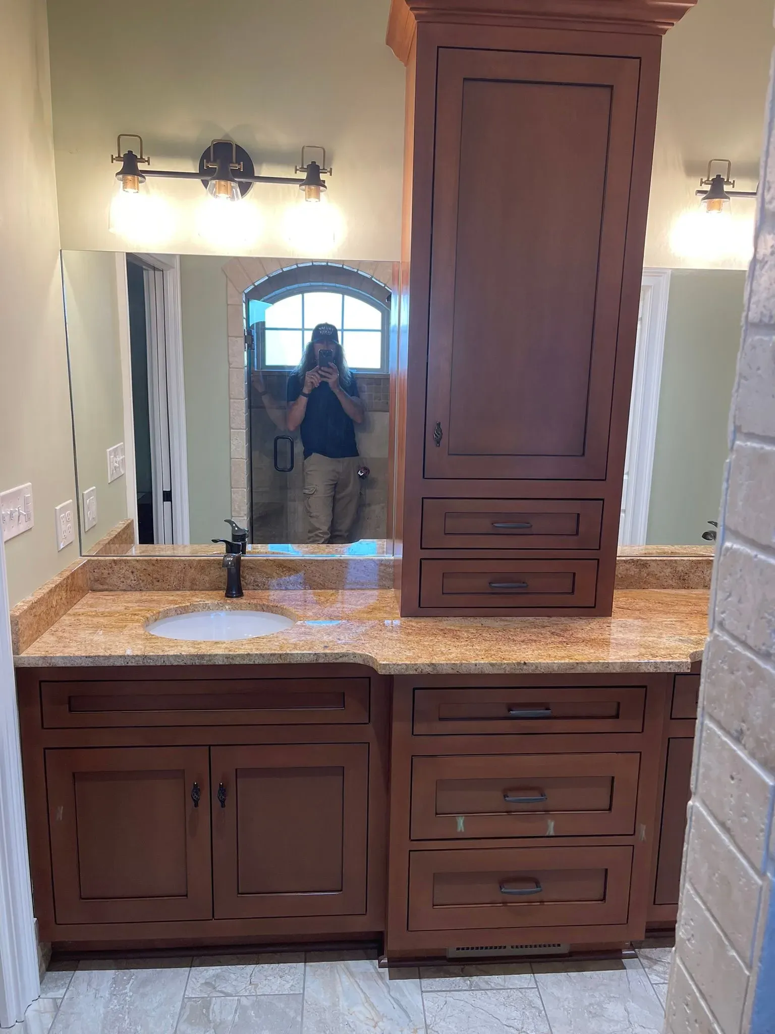 Bathroom vanity with dark wood cabinets, granite countertop, large mirror, and centered tower cabinet.